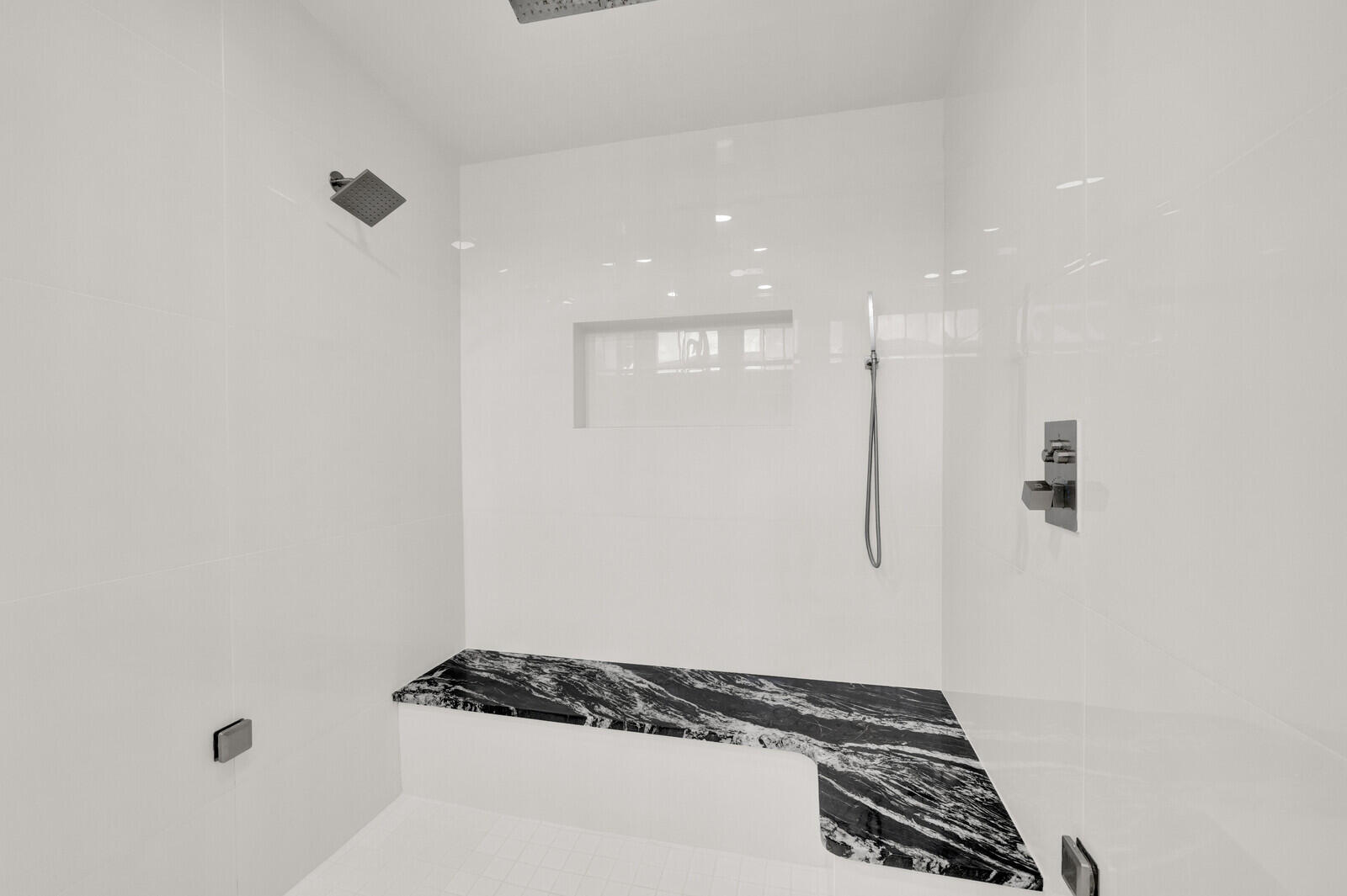 Spacious shower enclosure with white tile walls and a built-in black and white patterned stone bench