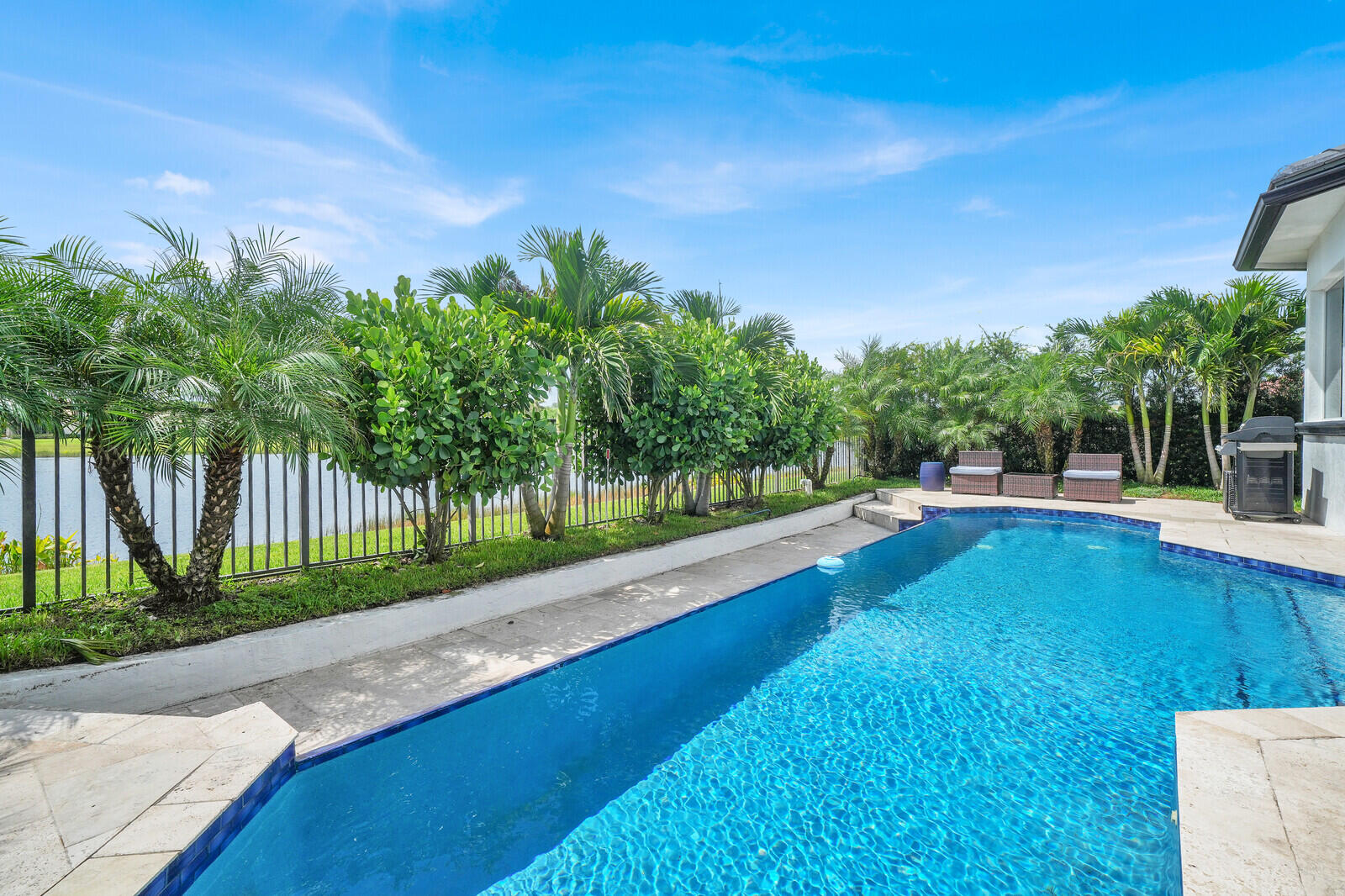 Inviting backyard pool with tile coping, concrete patio, and mature tropical landscaping