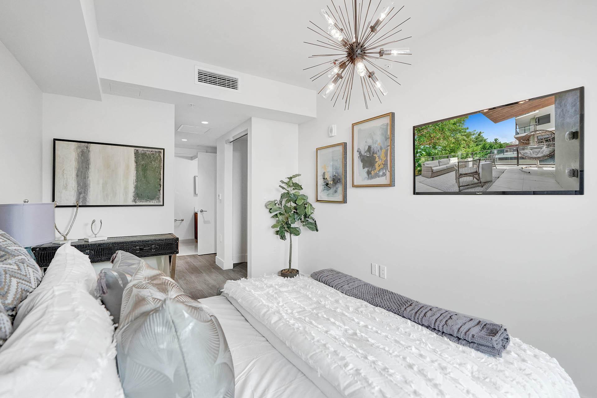 Bright and serene primary bedroom featuring crisp white bedding, wood-finish flooring, and abundant natural light