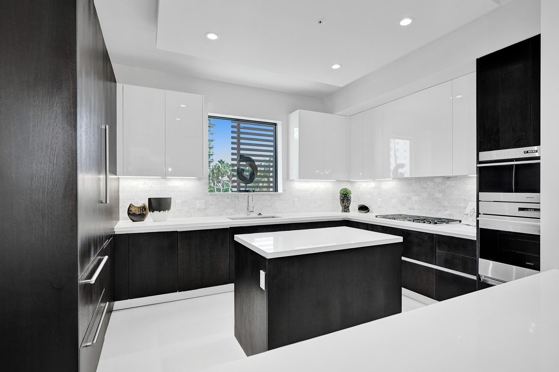 Modern kitchen featuring dark wood-finish lower cabinetry, white high-gloss upper cabinetry, a central island with a white countertop, stainless steel appliances, and a mosaic tile backsplash