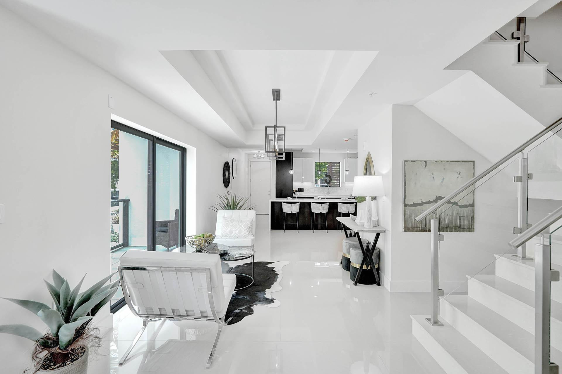 Open-concept interior featuring high ceilings, white tile flooring, and a modern glass and metal staircase