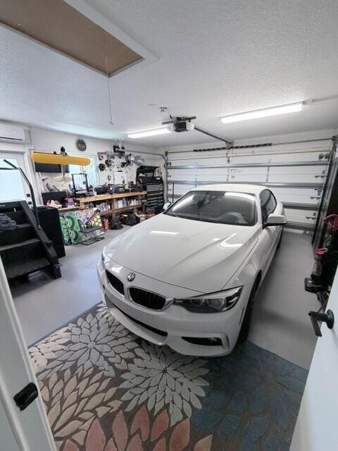 Attached two-car garage featuring a sectional garage door, overhead fluorescent lighting, a window-mounted air conditioning unit, and attic access