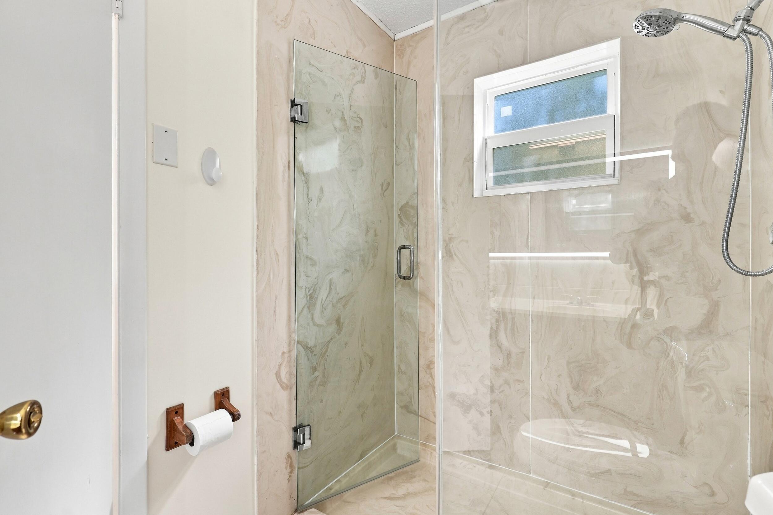 Updated shower featuring glass doors, tiled walls, and a window for natural light.