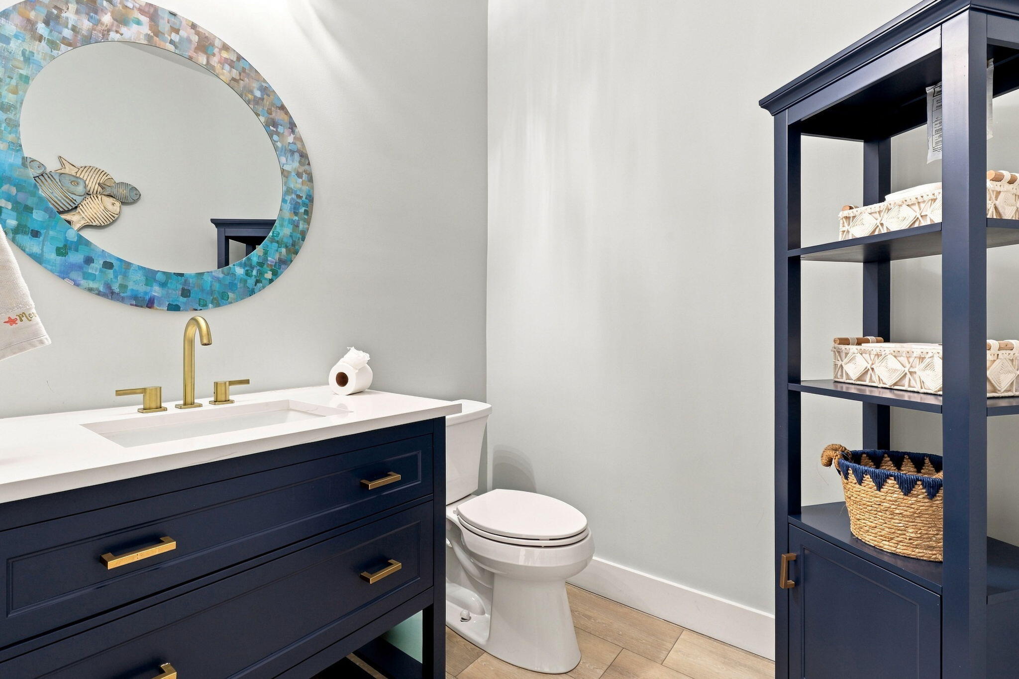 Navy vanity with gold-tone hardware and fixtures, white countertop with an integrated sink and a coordinating freestanding shelving unit
