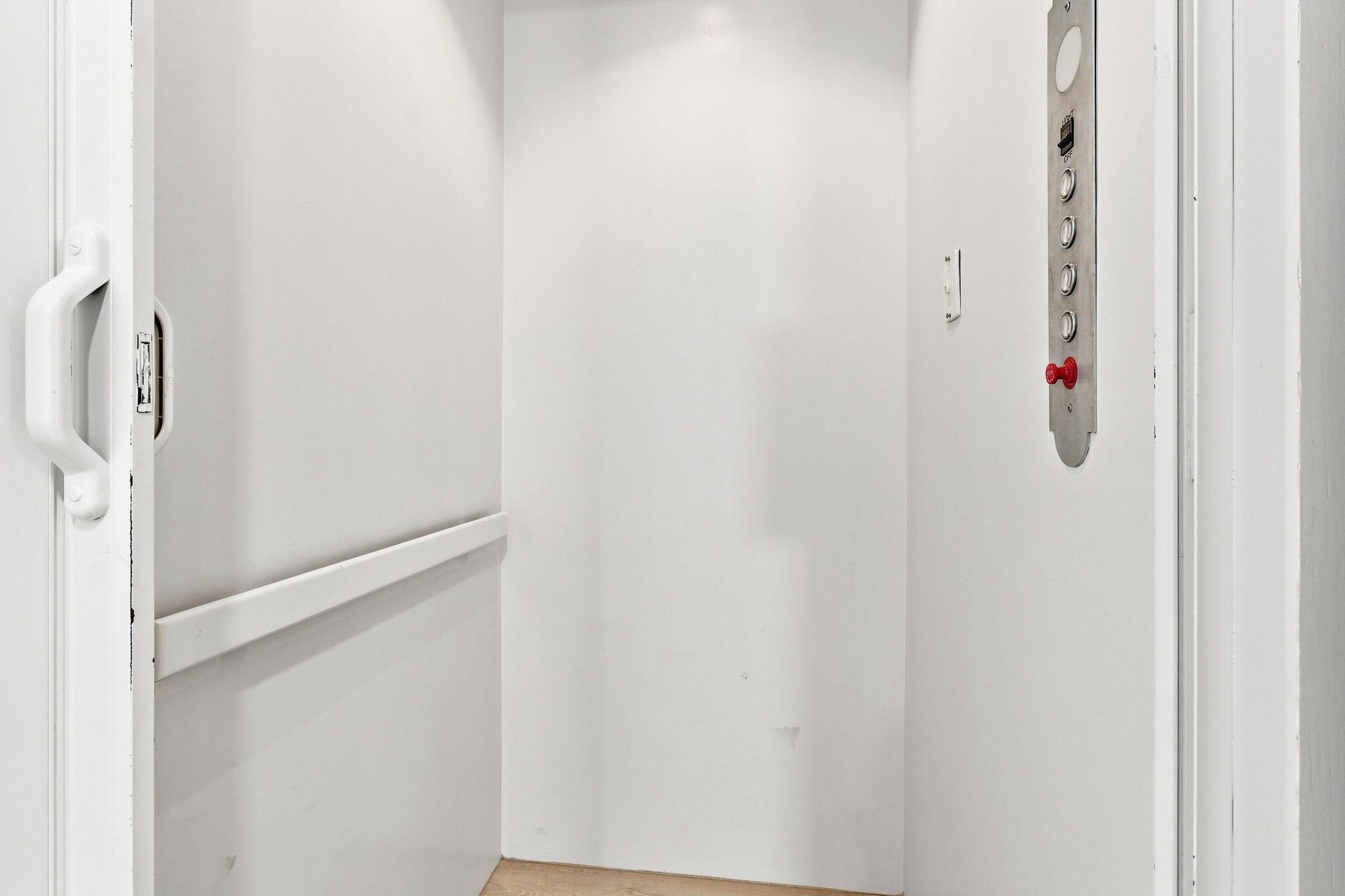 Interior elevator with luxury vinyl flooring, recessed ceiling lighting and a metal control panel featuring red emergency stop button