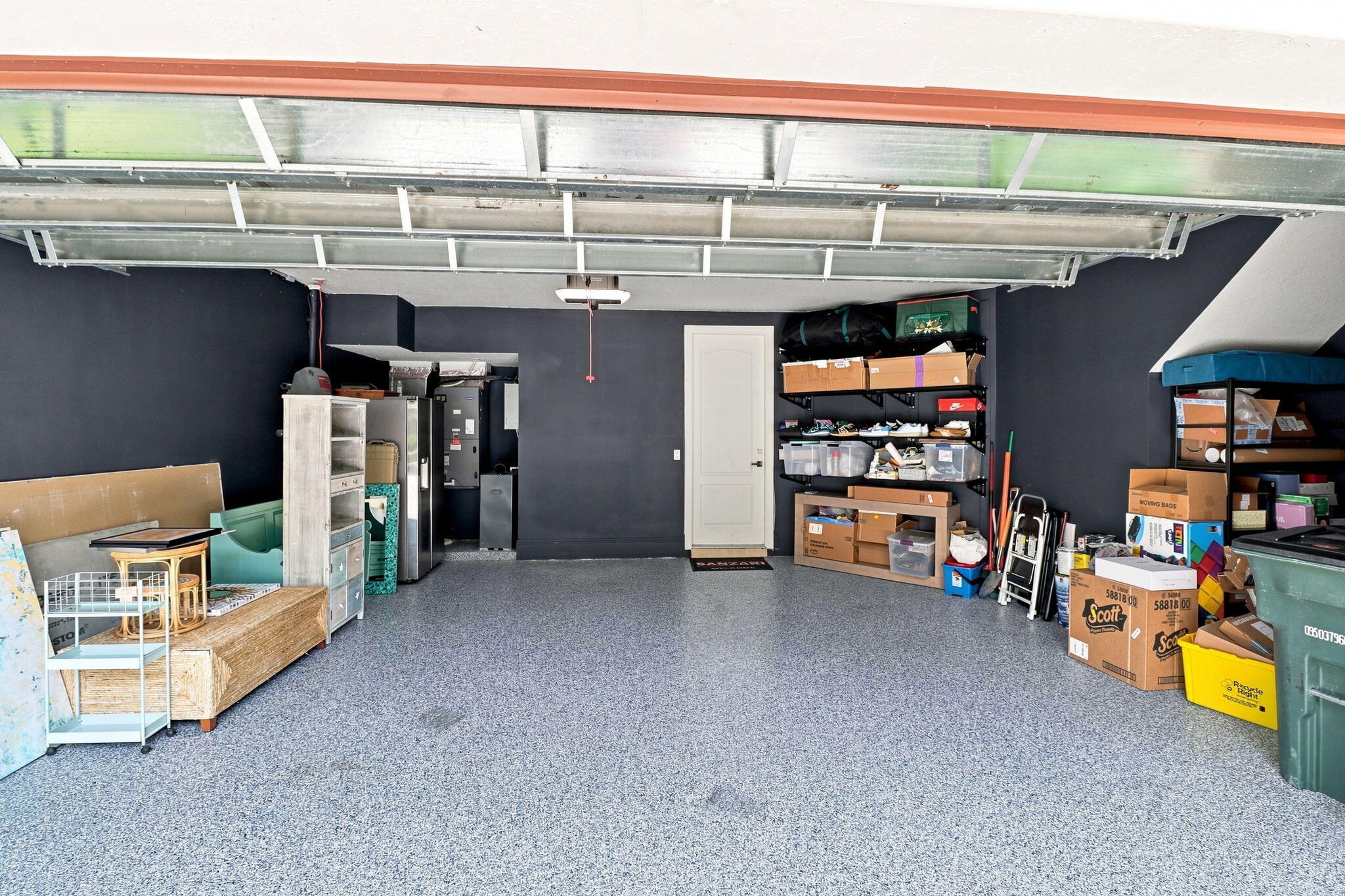 Attached garage featuring a light speckled floor coating, dark-toned walls and a white interior door