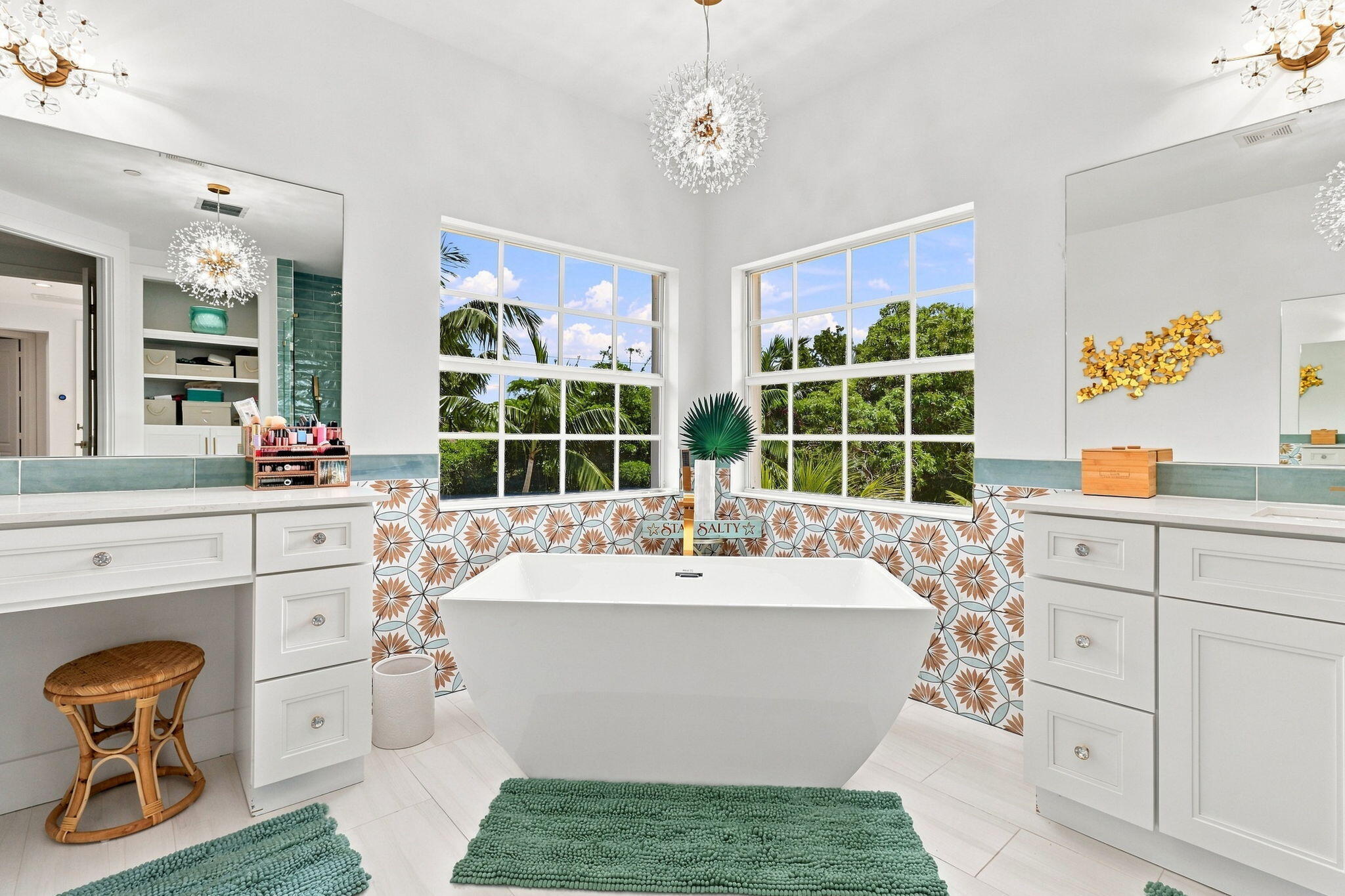 Freestanding soaking tub with patterned tile surround, dual vanity areas featuring white cabinetry and two large windows