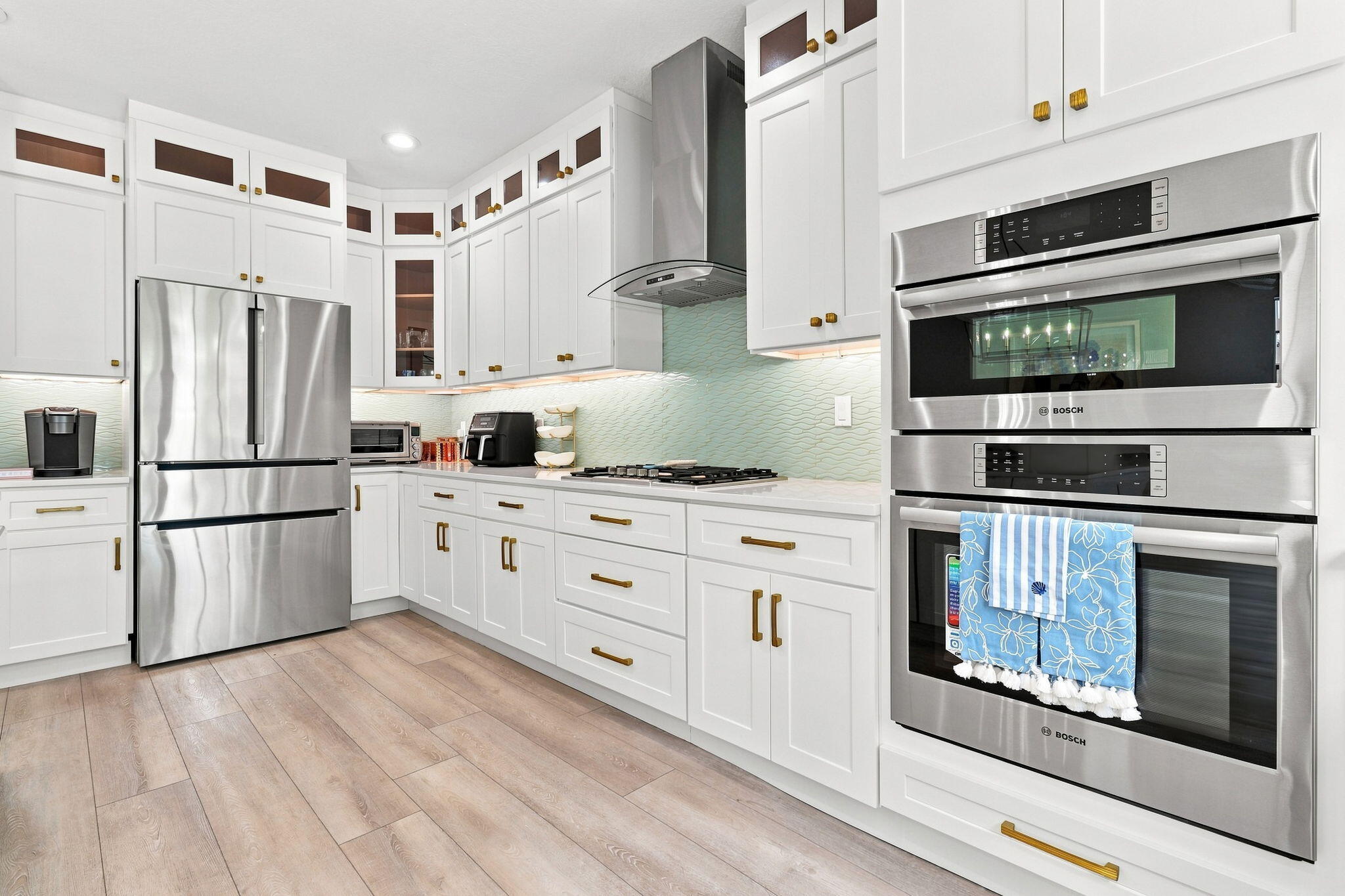 White cabinetry with gold-finish hardware, light-toned luxury vinyl flooring, stainless steel appliances and a tiled backsplash
