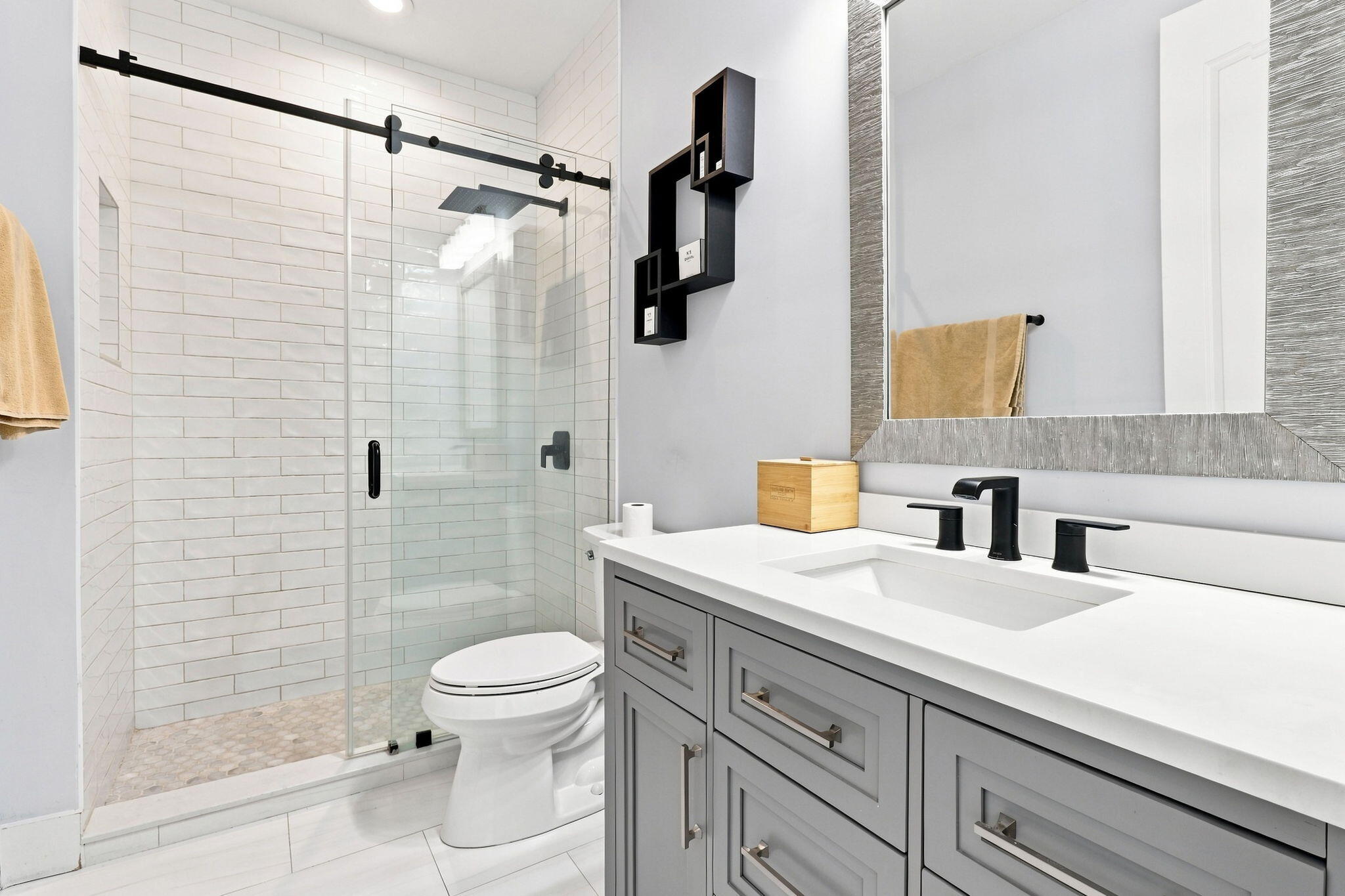Glass-enclosed shower with subway tile surround and dark hardware, vanity with a white countertop and undermount sink and tile flooring