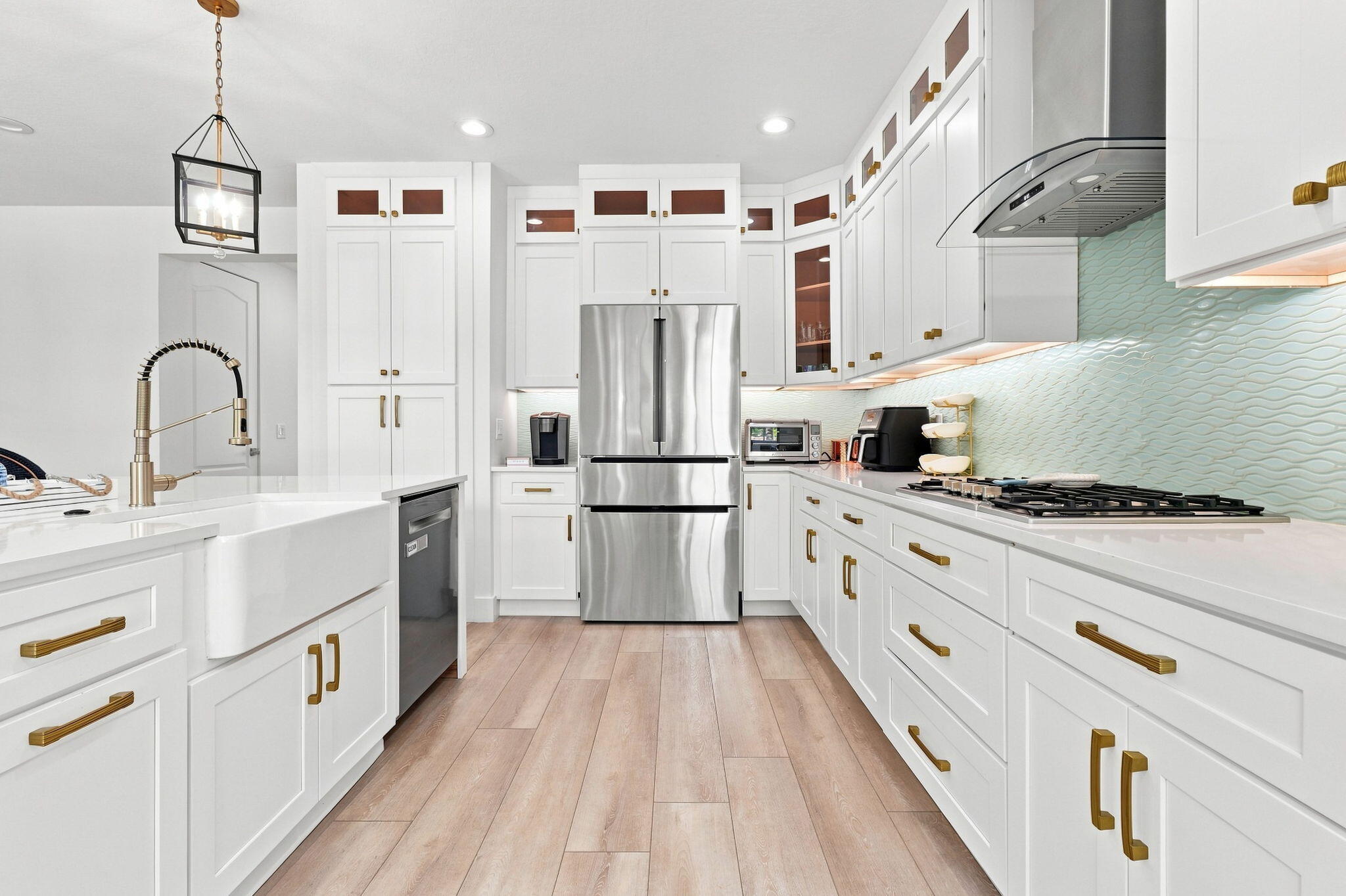 White shaker cabinetry, luxury vinyl flooring, stainless steel appliances, white countertops and a textured tile backsplash