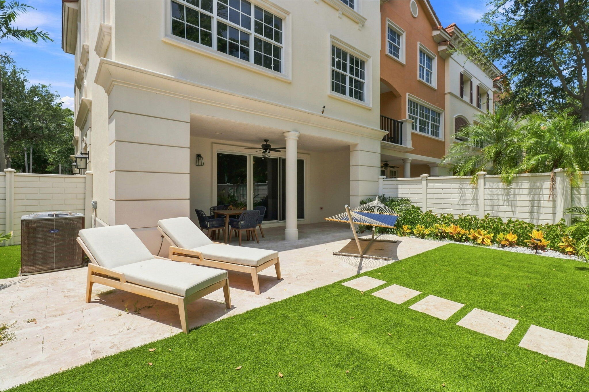 Expansive outdoor living area featuring a lanai, paved hardscaping, a manicured turf lawn with stepping stones and mature tropical landscaping