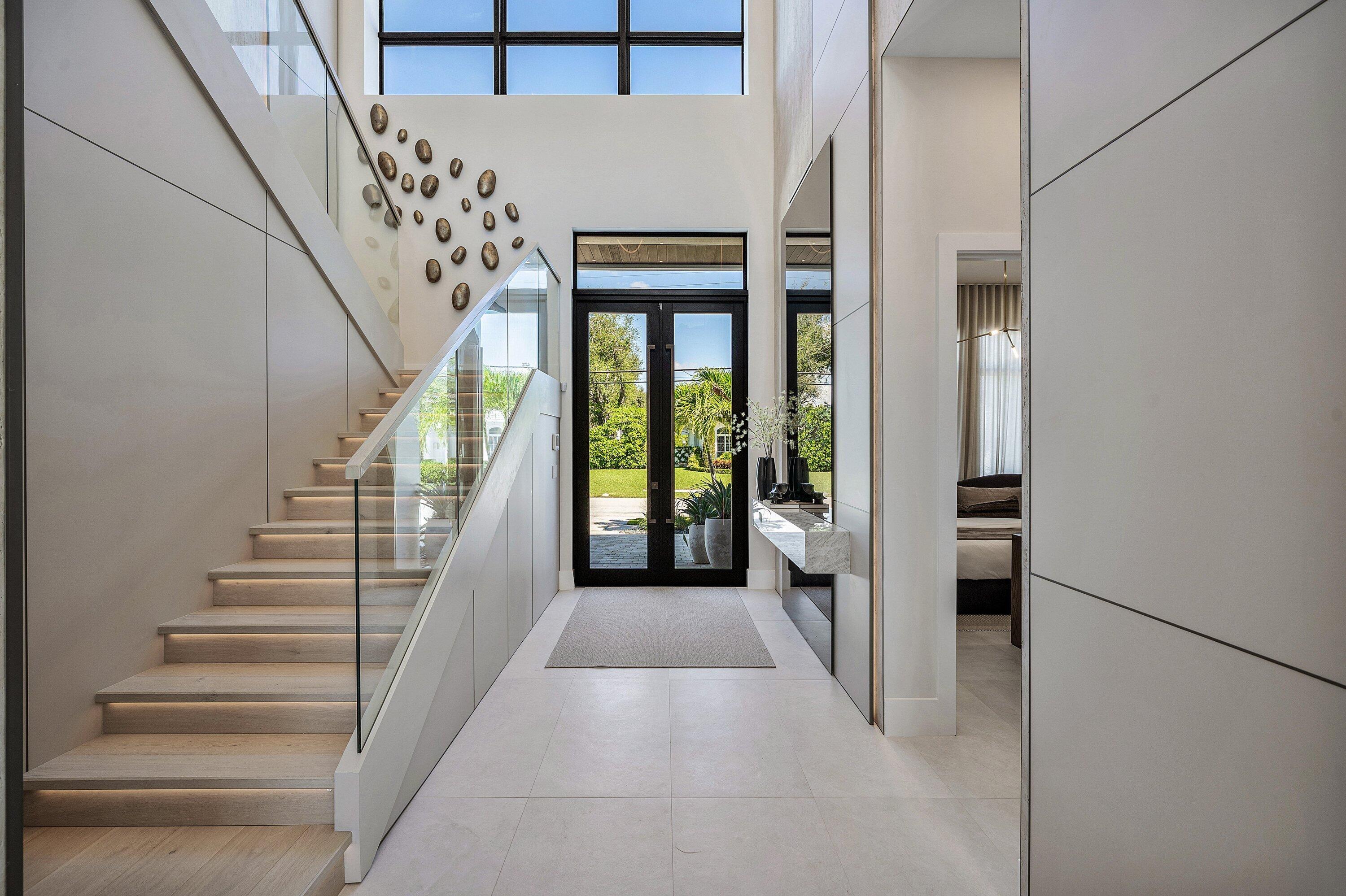 Grand entryway featuring a floating stone console, recessed lighting, glass railing staircase, and light-toned flooring