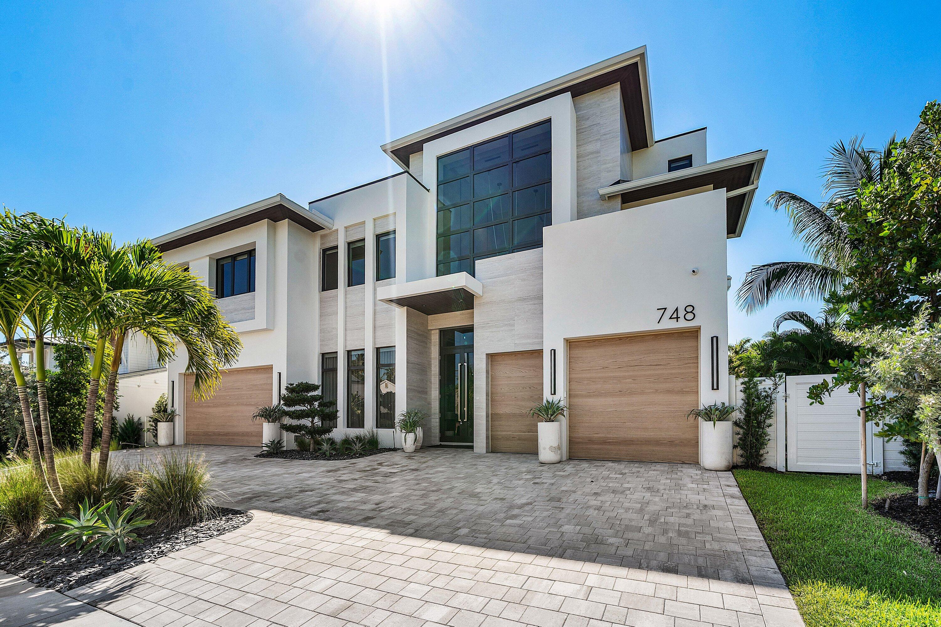 Contemporary stucco exterior with a flat roofline, wood-finish garage doors, large dark-framed windows, and a paver driveway