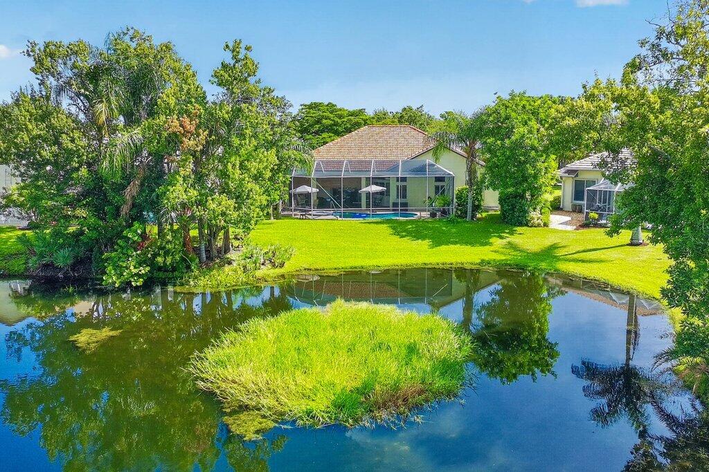 Expansive waterfront property with a screened-in pool enclosure, lush green lawn, mature trees, and a separate screened-in patio structure