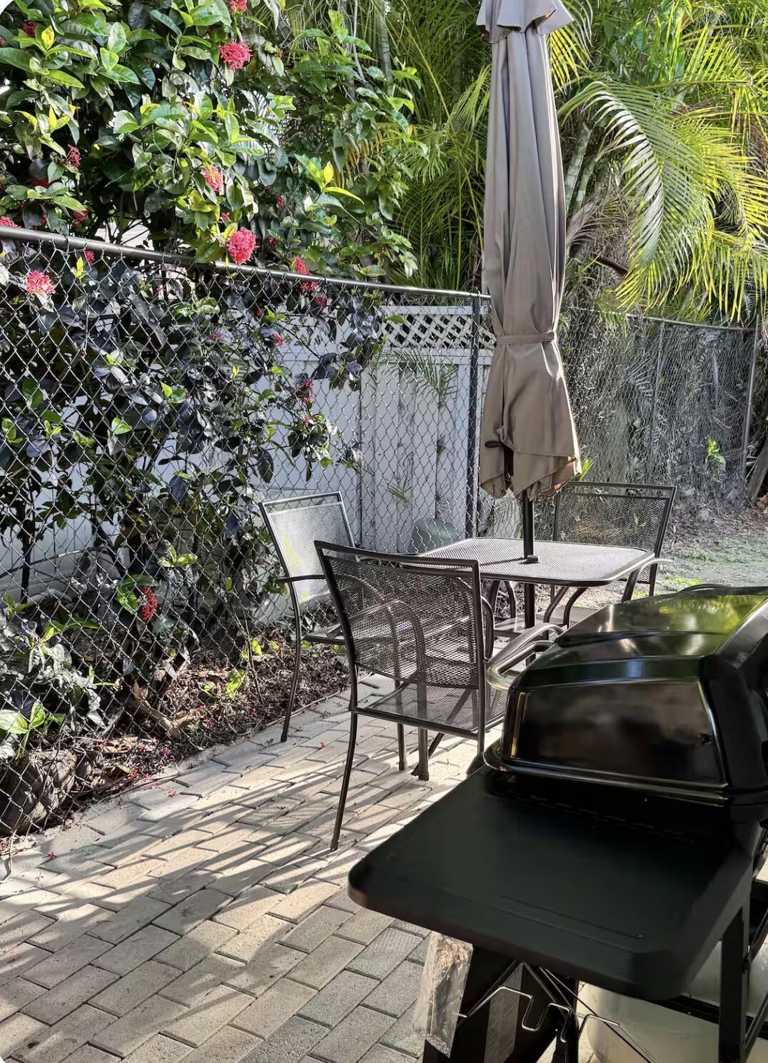 patio with lush tropical landscaping, brick pavers, outdoor dining area, and grill.
