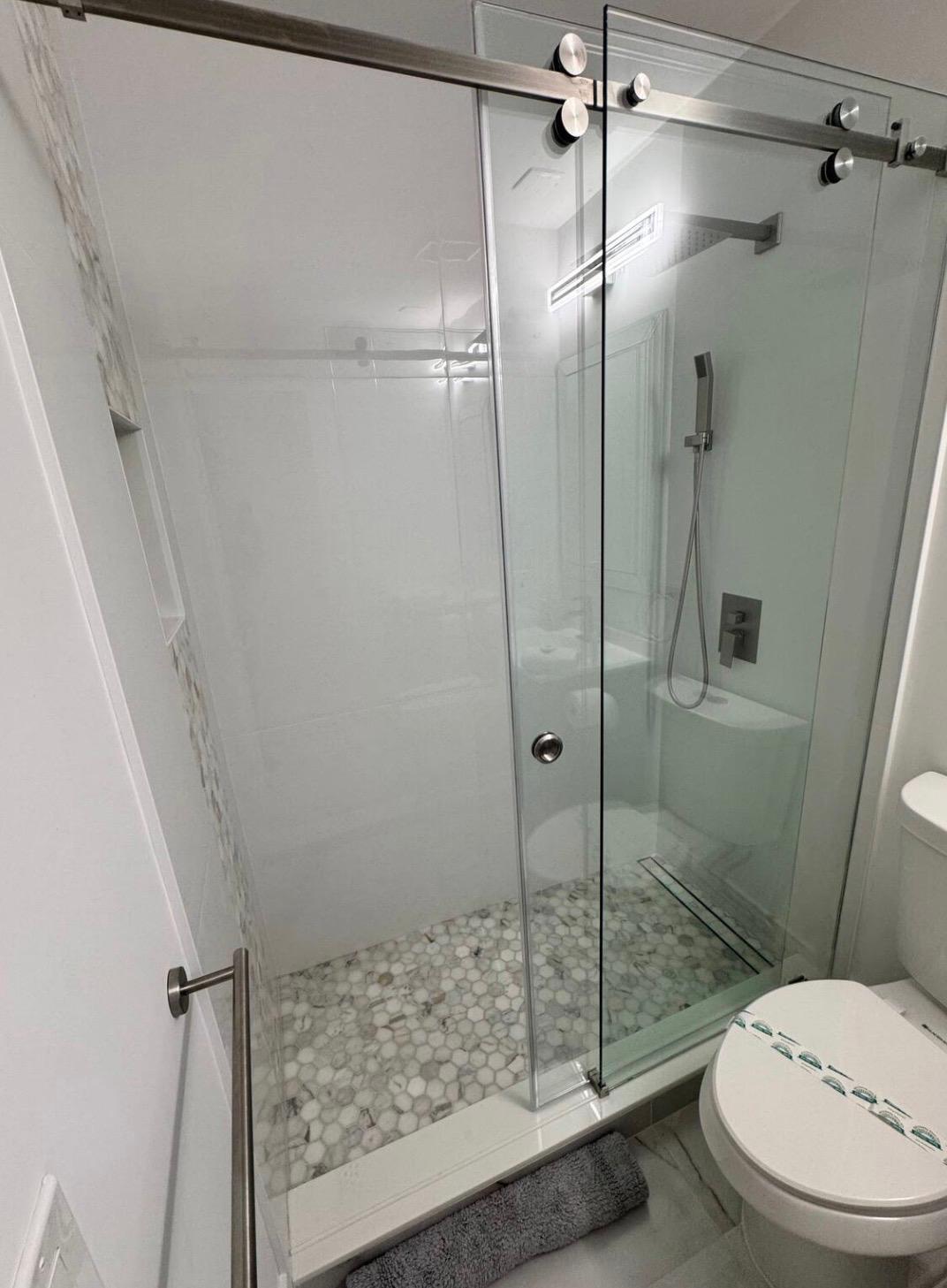 Frameless glass shower enclosure with sliding door, pebble tile shower floor, and a linear shower drain Frameless glass shower enclosure with sliding door, pebble tile shower floor, and a linear shower drain