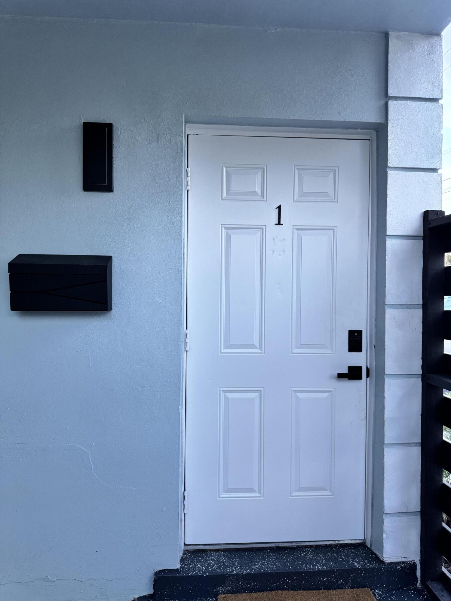 Panel door with black hardware, flanked by a black wall sconce and black mailbox Panel door with black hardware, flanked by a black wall sconce and black mailbox