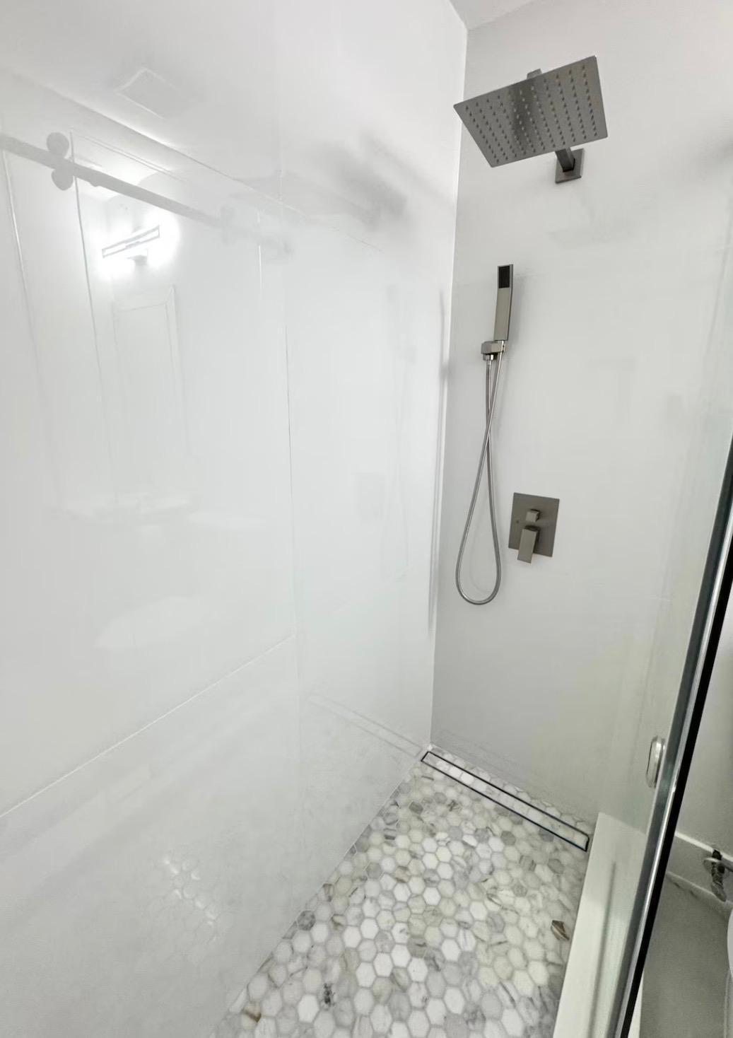 Walk-in shower with hexagonal floor tile, linear drain, and a rain showerhead with an additional handheld shower fixture