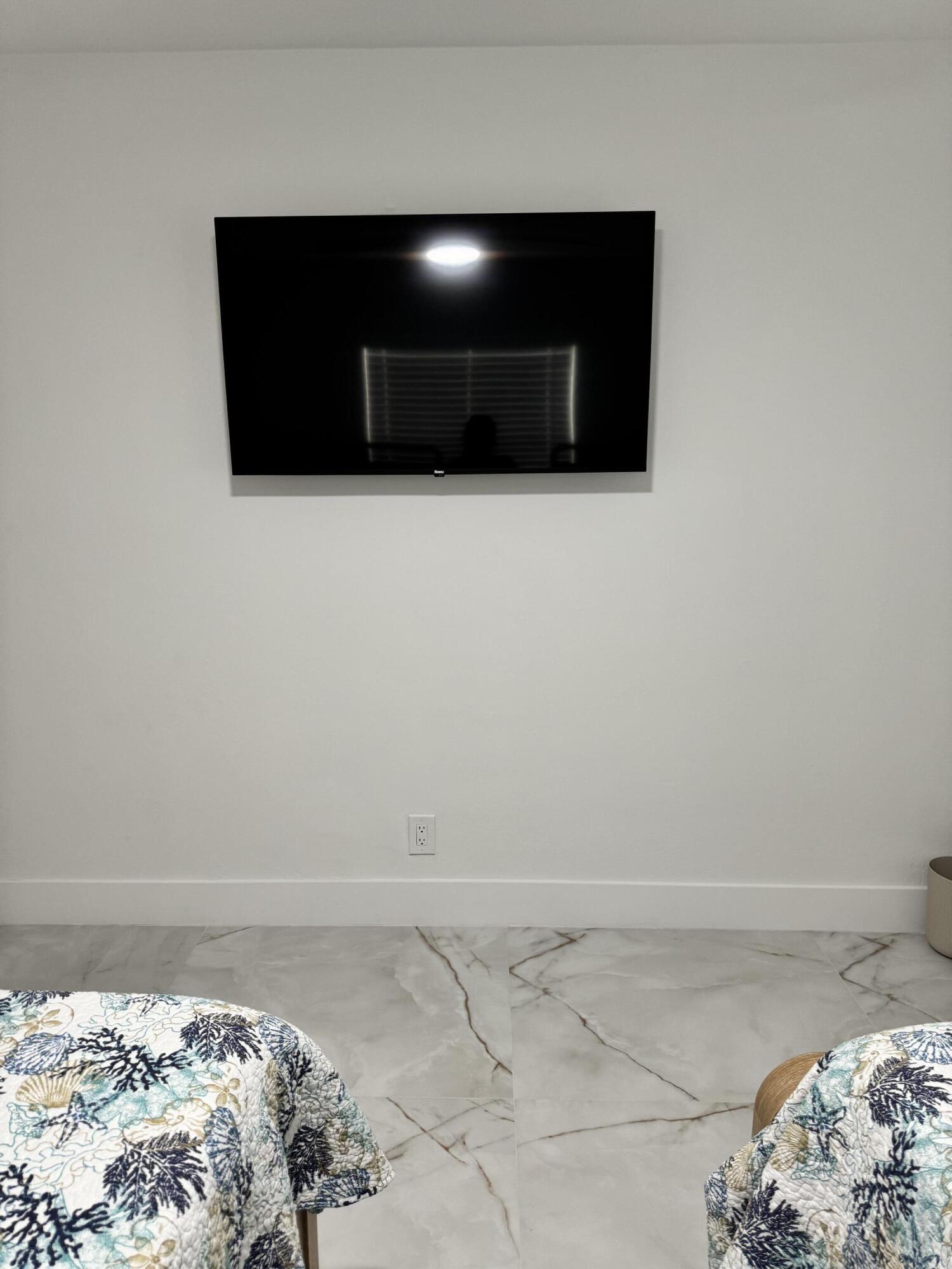 Spacious bedroom featuring a wall-mounted TV, elegant marble-look tile flooring, and a clean, modern design