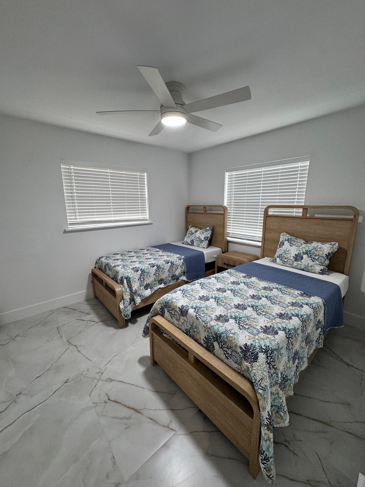 White tile flooring with grey veining, two windows with blinds, and a ceiling fan with integrated lighting