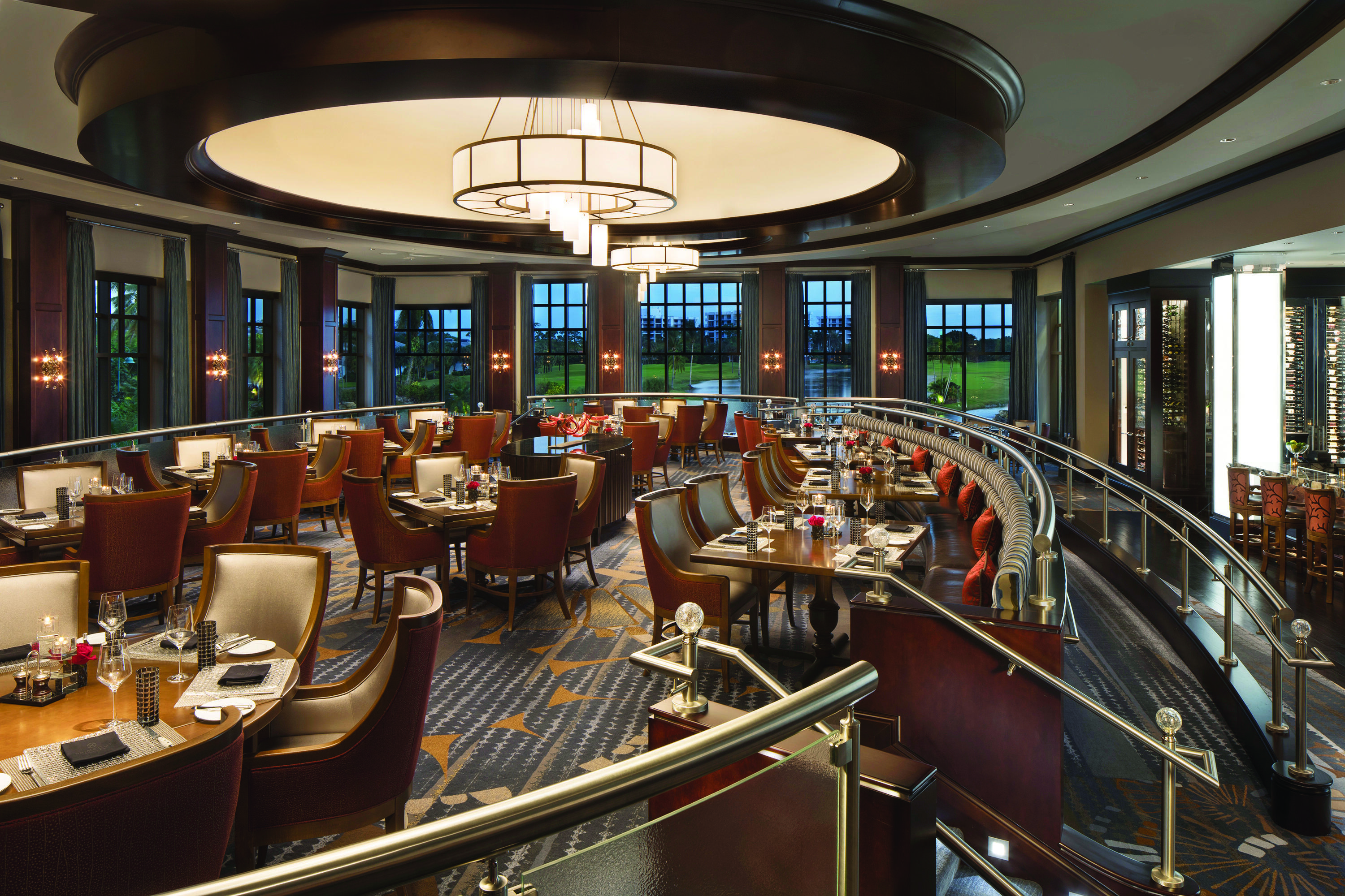 Tiered dining area with a curved stainless steel railing, wood-finish flooring, recessed ceiling lighting, and multiple window exposures