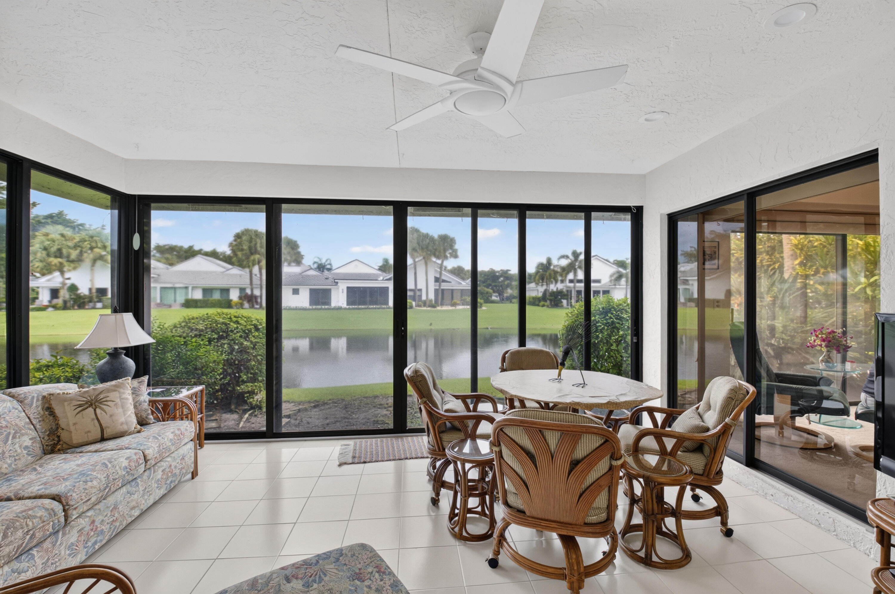 Screened lanai featuring expansive glass panels, white tile flooring, and a ceiling fan
