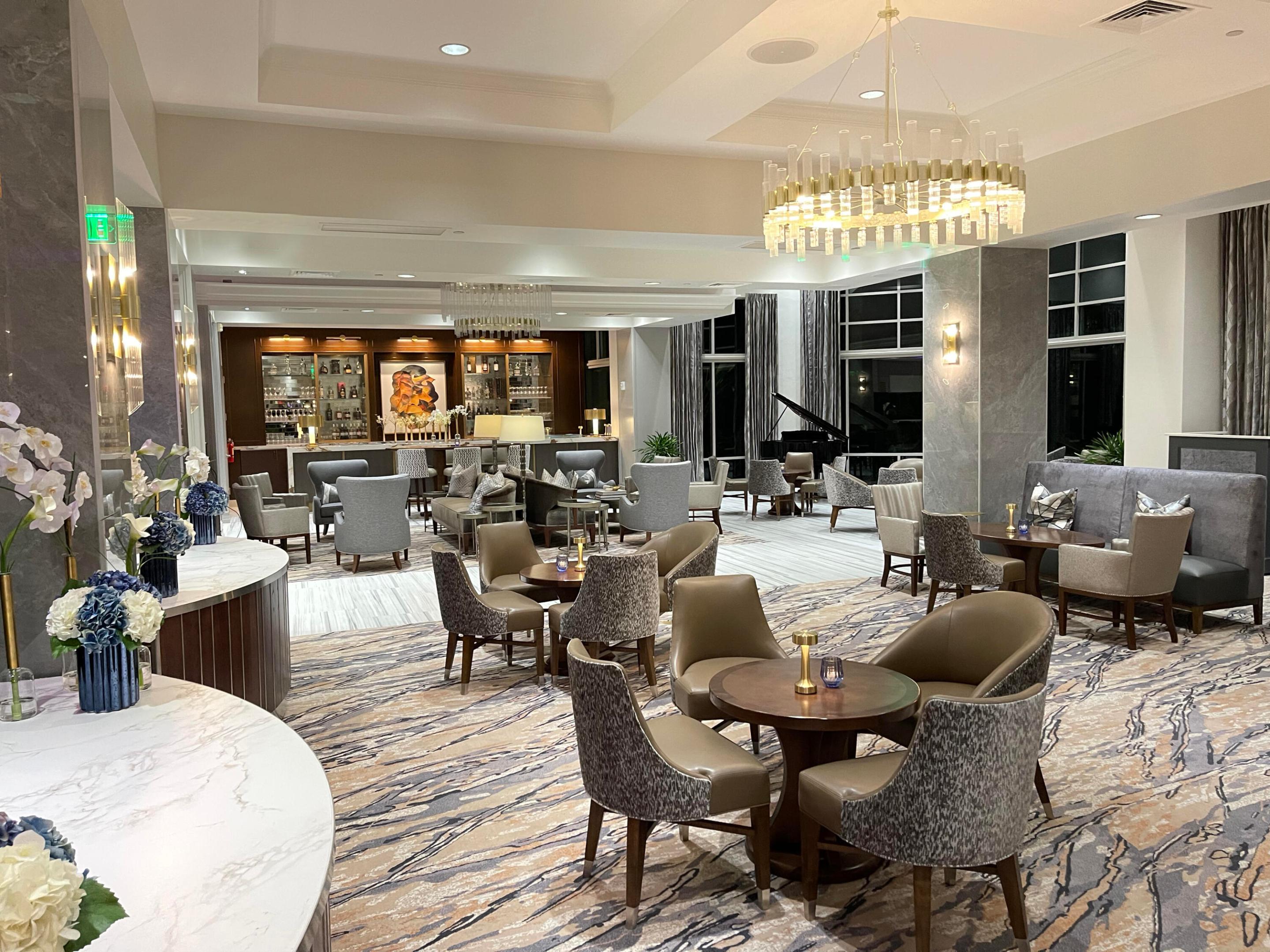 Spacious common area featuring a full-service bar, grand piano, decorative chandelier, and large windows