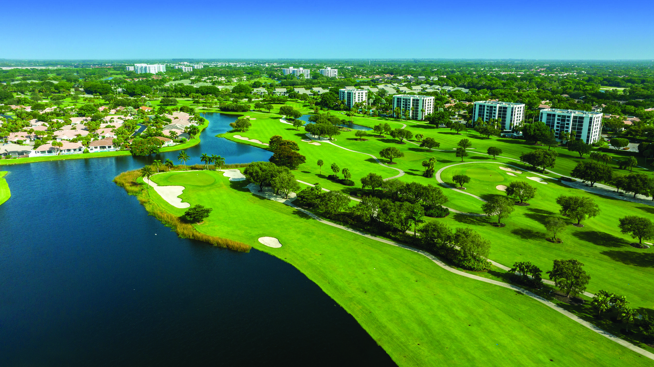 Expansive golf course with manicured greens and sand traps, bordered by a large water feature