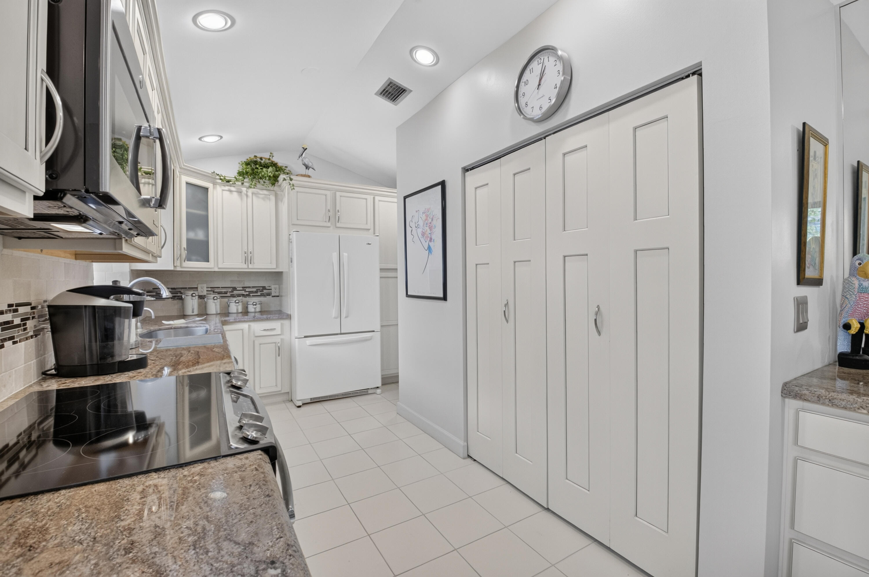 Vaulted ceiling, recessed lighting, white cabinetry, tile flooring, and a patterned backsplash