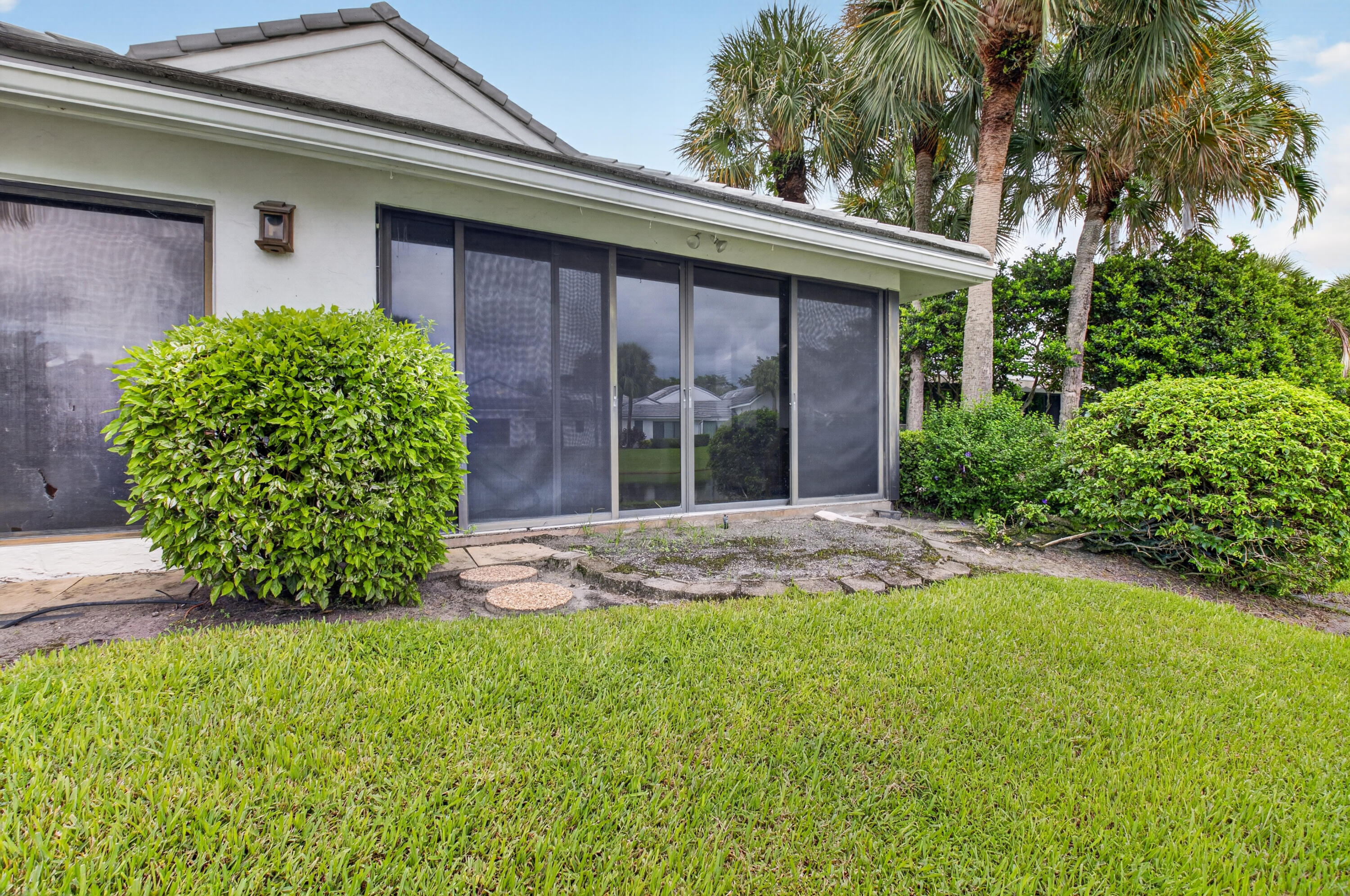 Modern residence showcasing expansive manicured lawn, mature palm trees, and professionally landscaped foundation plantings