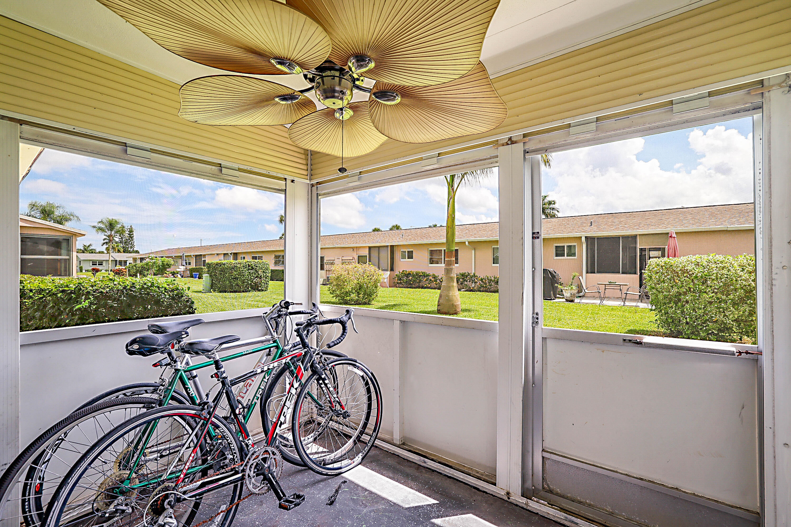Screened porch featuring a ceiling fan with palm-leaf style blades, exterior siding, and a landscaped outdoor area