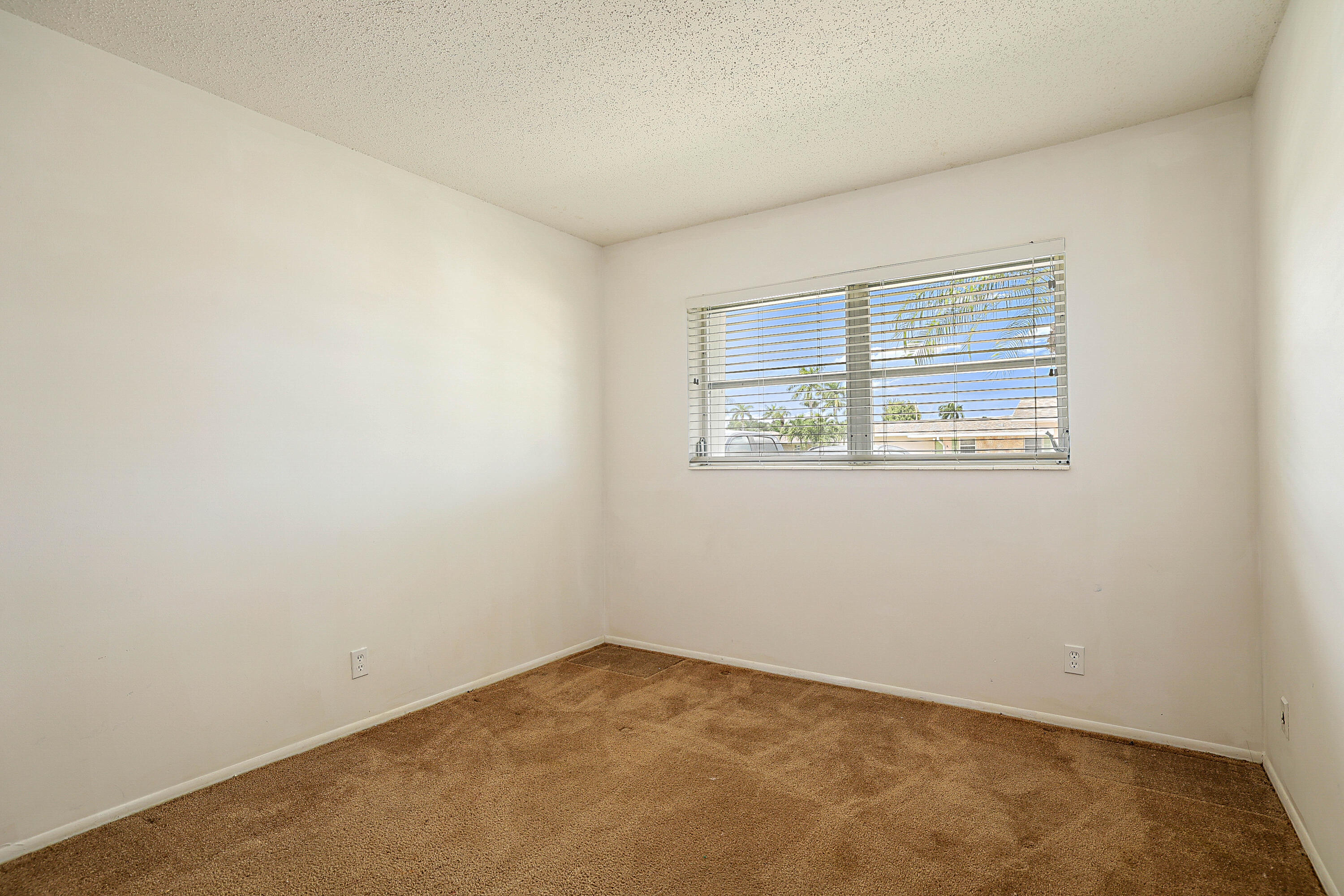 Neutral wall paint, textured ceiling, window with blinds, and carpeted flooring