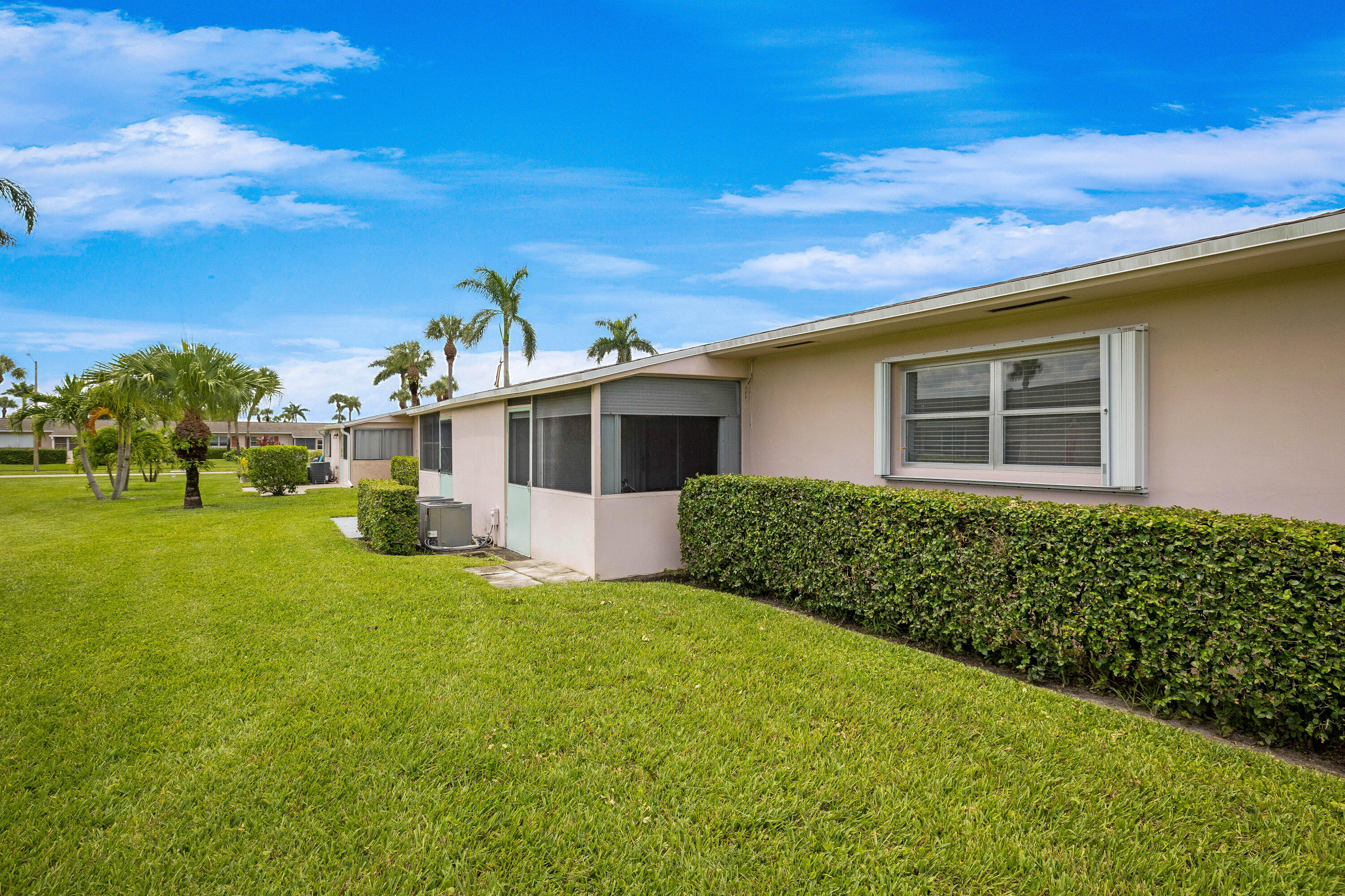 Screened patio, stucco exterior, window with hurricane shutters, manicured lawn, and mature palm trees