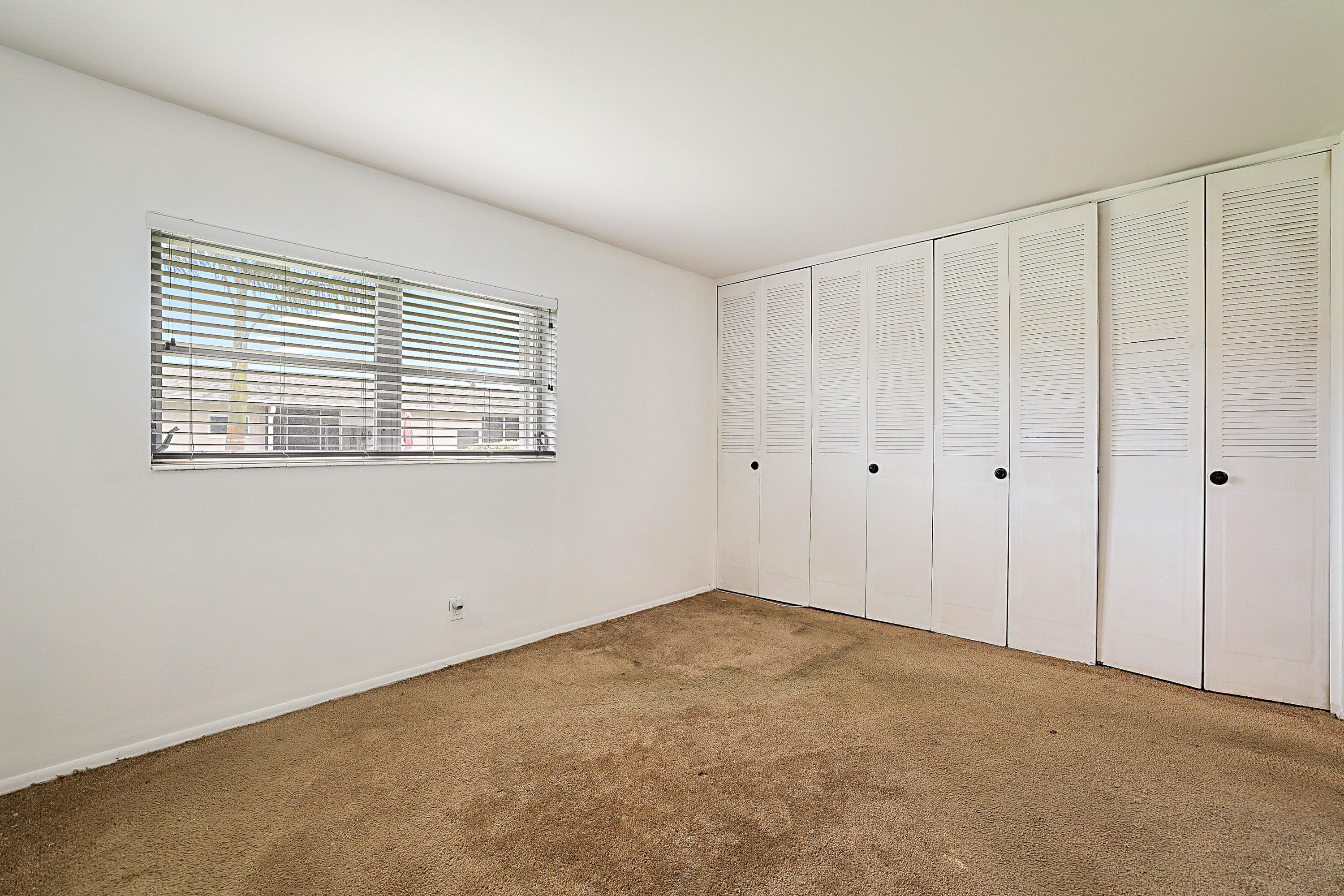 White walls, horizontal window blinds, and built-in louvered closet doors