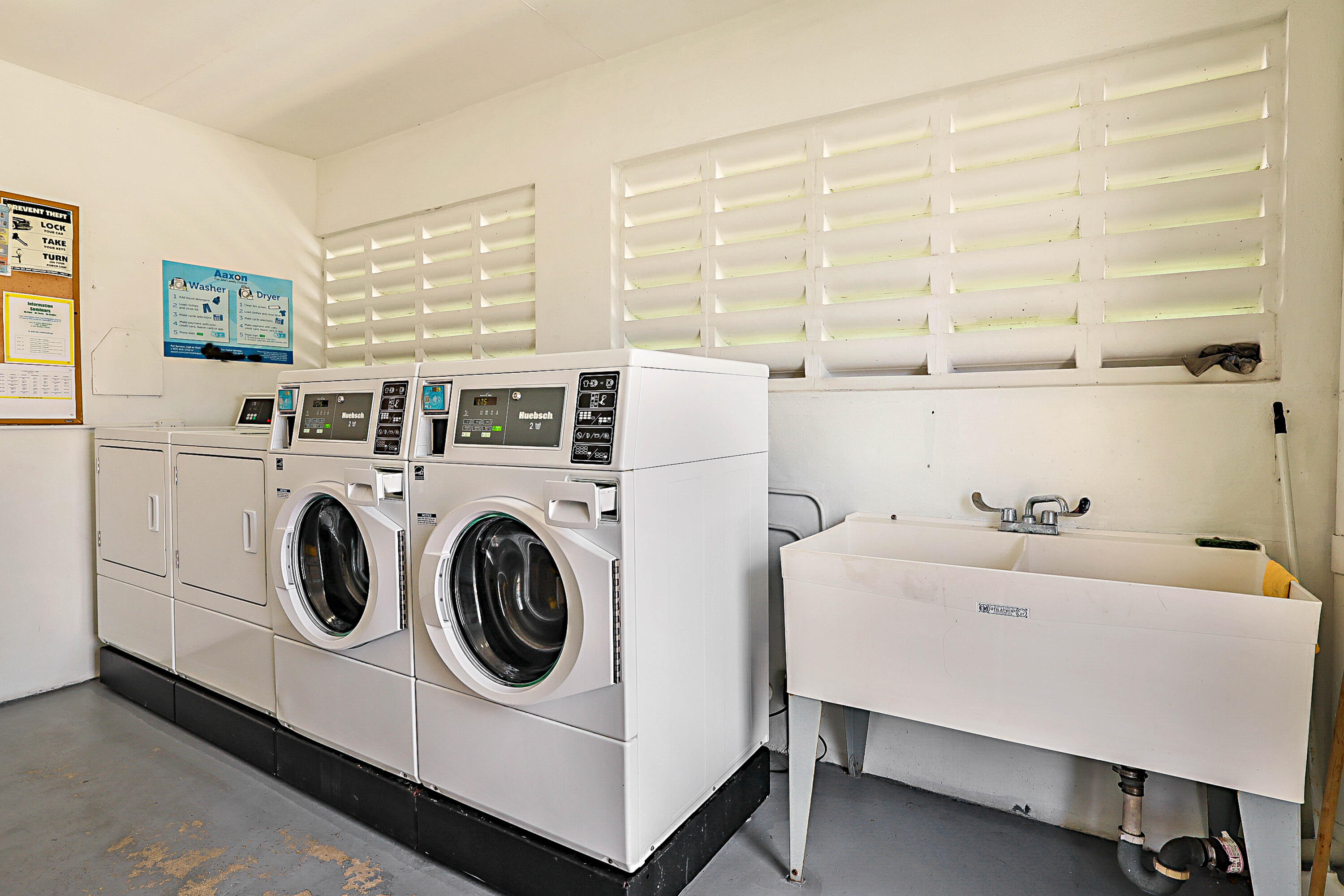 Dedicated laundry facility featuring multiple front-load washers, top-load dryers, and a utility sink