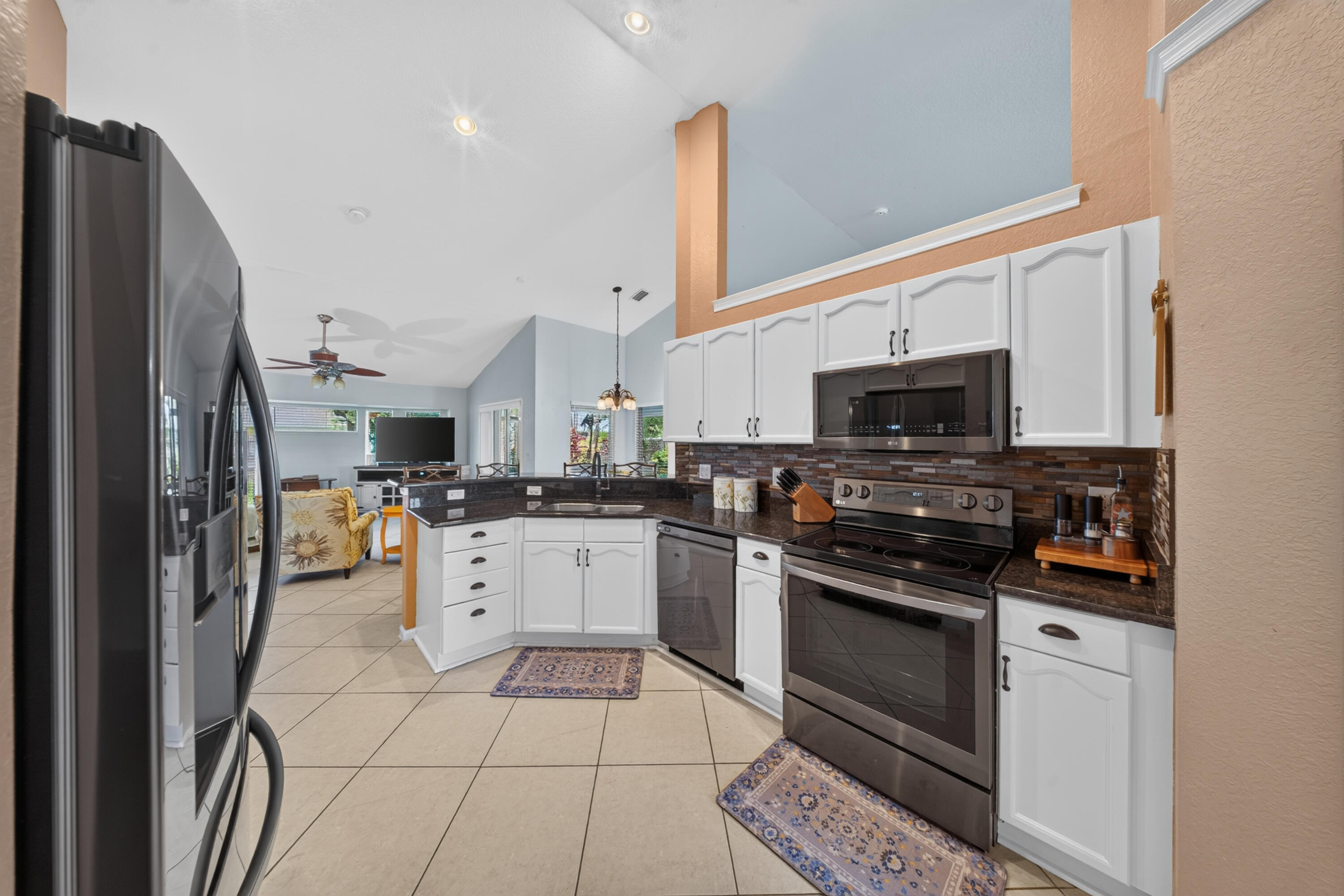 Kitchen featuring white cabinetry, dark countertops, dark tile backsplash, stainless steel appliances, and tile flooring