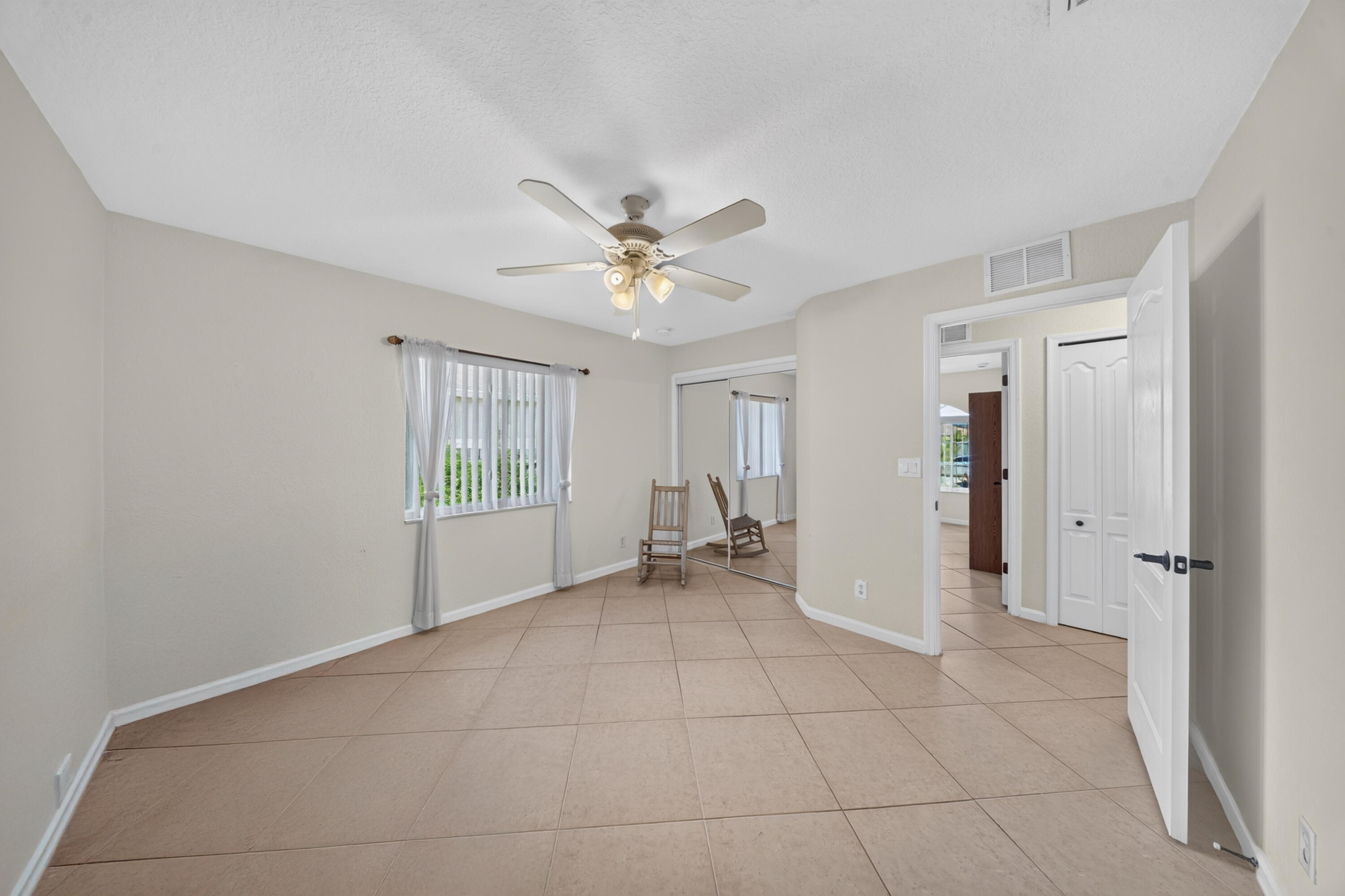 Spacious room featuring tile flooring, a ceiling fan with integrated lighting, and a window with vertical blinds