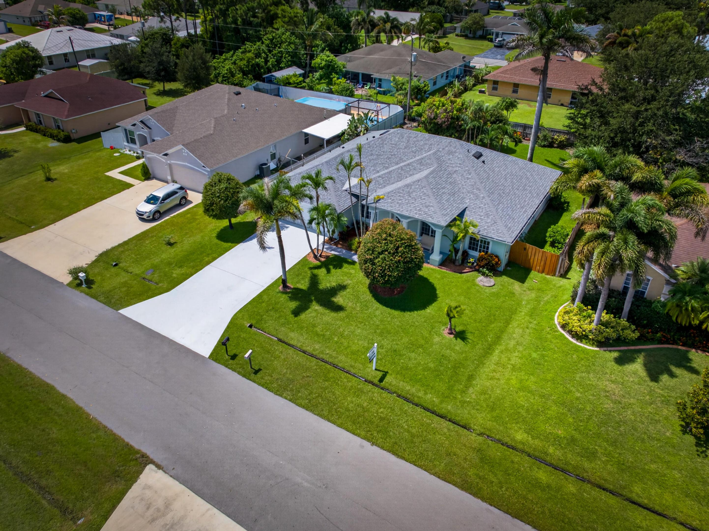 Paved driveway, attached garage, well-maintained lawn, mature landscaping, and privacy fencing