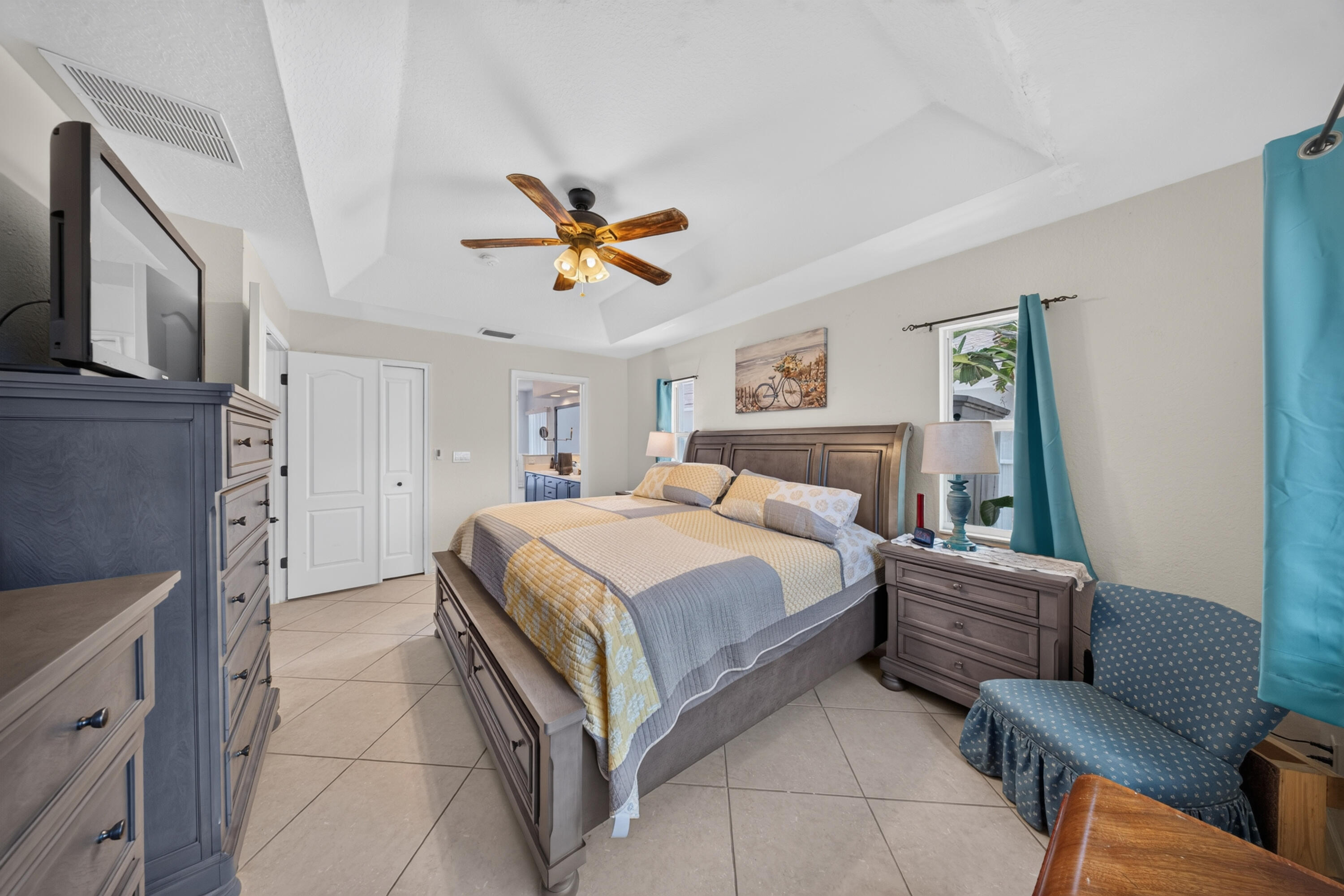 Recessed tray ceiling with a built-in ceiling fan, white paneled doors, and large format tile flooring