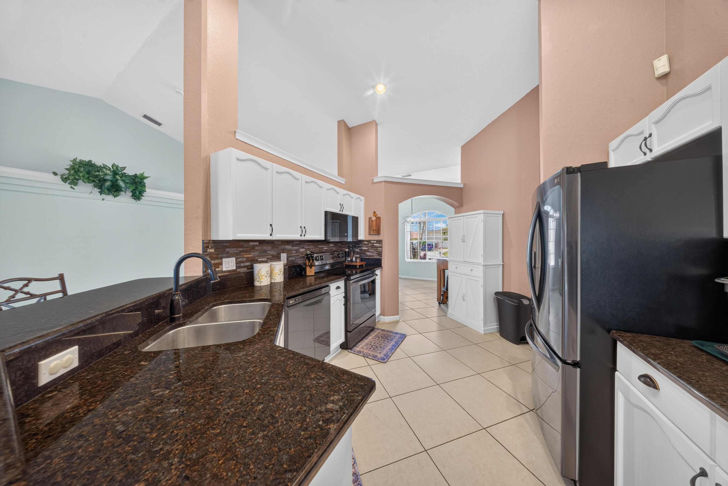 Kitchen featuring vaulted ceilings, white cabinetry with crown molding, dark stone countertops, stainless steel appliances, and a tile backsplash
