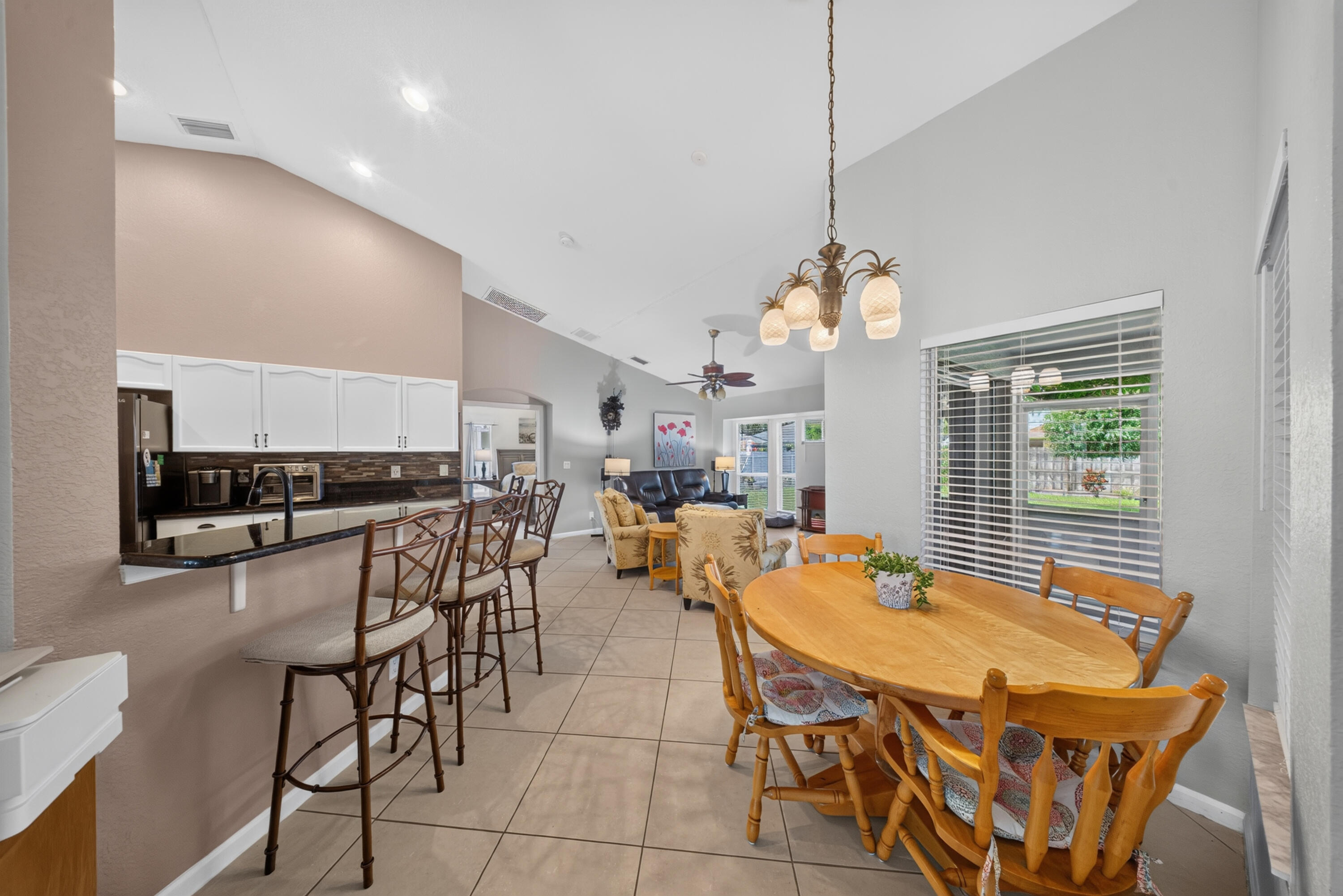 Vaulted ceilings, tiled flooring, white cabinetry, black countertops, and a decorative chandelier