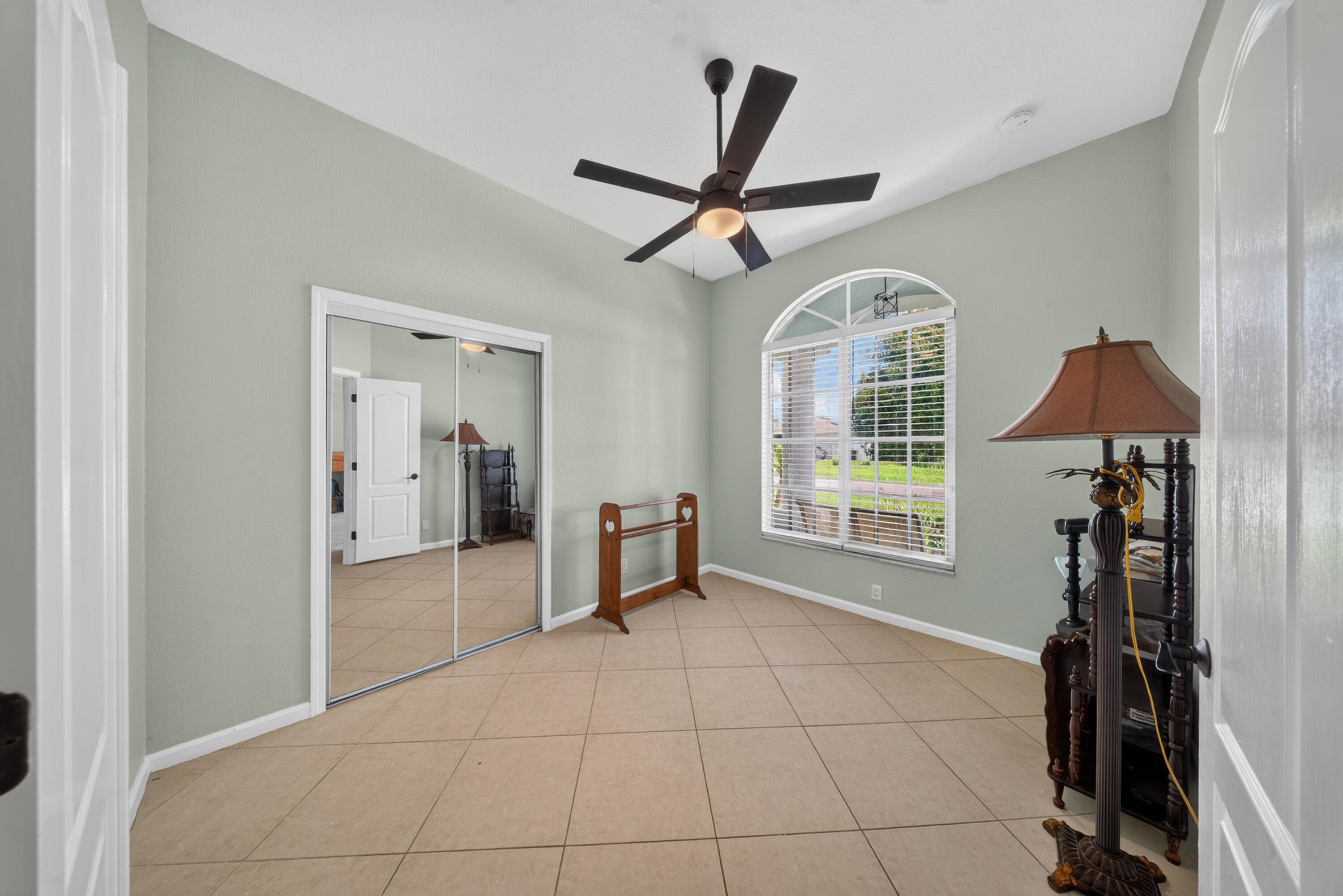 Vaulted ceiling with a ceiling fan, arched window, tiled flooring, and mirrored closet doors