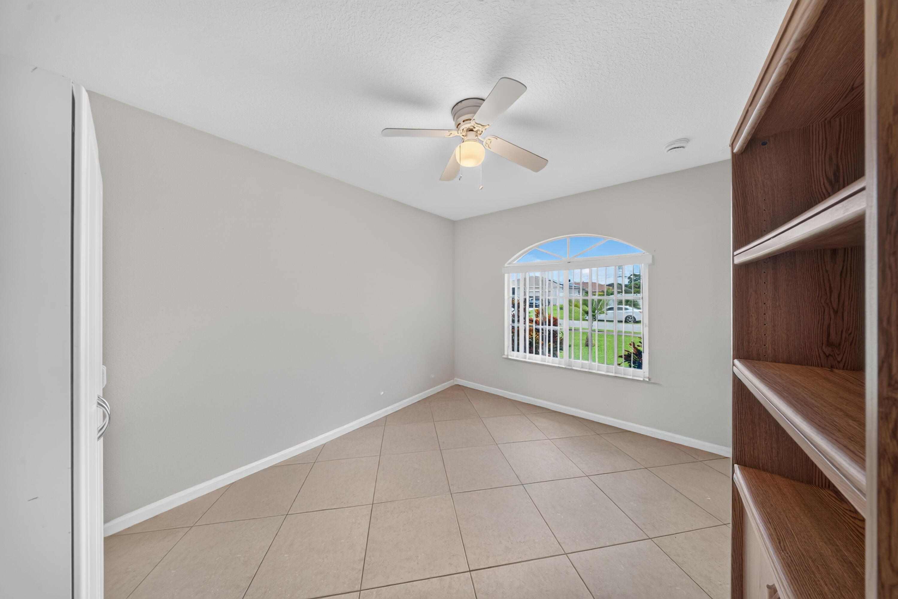 Arched window with blinds, ceiling fan with light fixture, light gray wall paint, and tile flooring