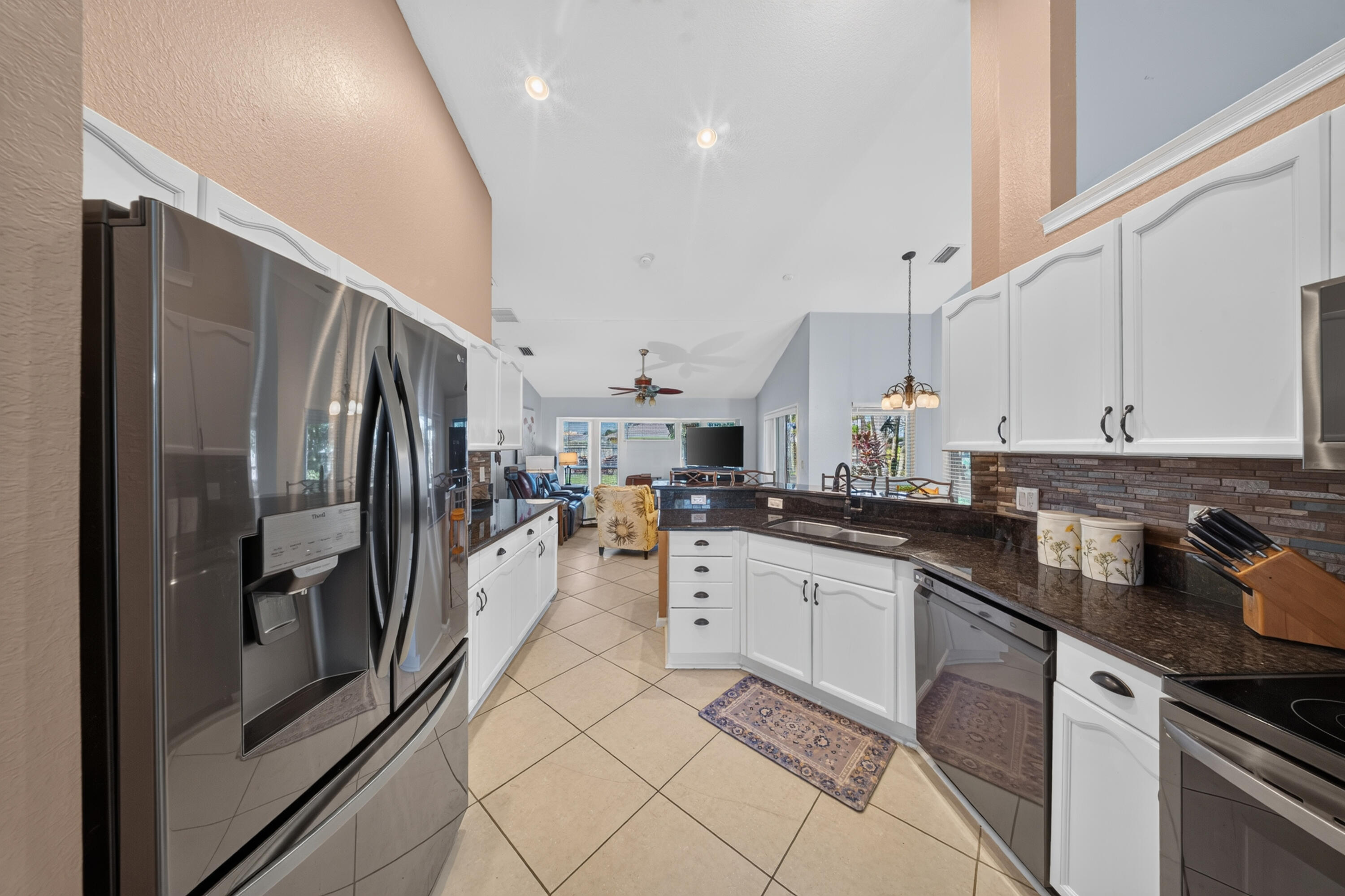 Kitchen featuring vaulted ceilings, stainless steel appliances, white cabinetry, dark stone countertops, and a mosaic tile backsplash