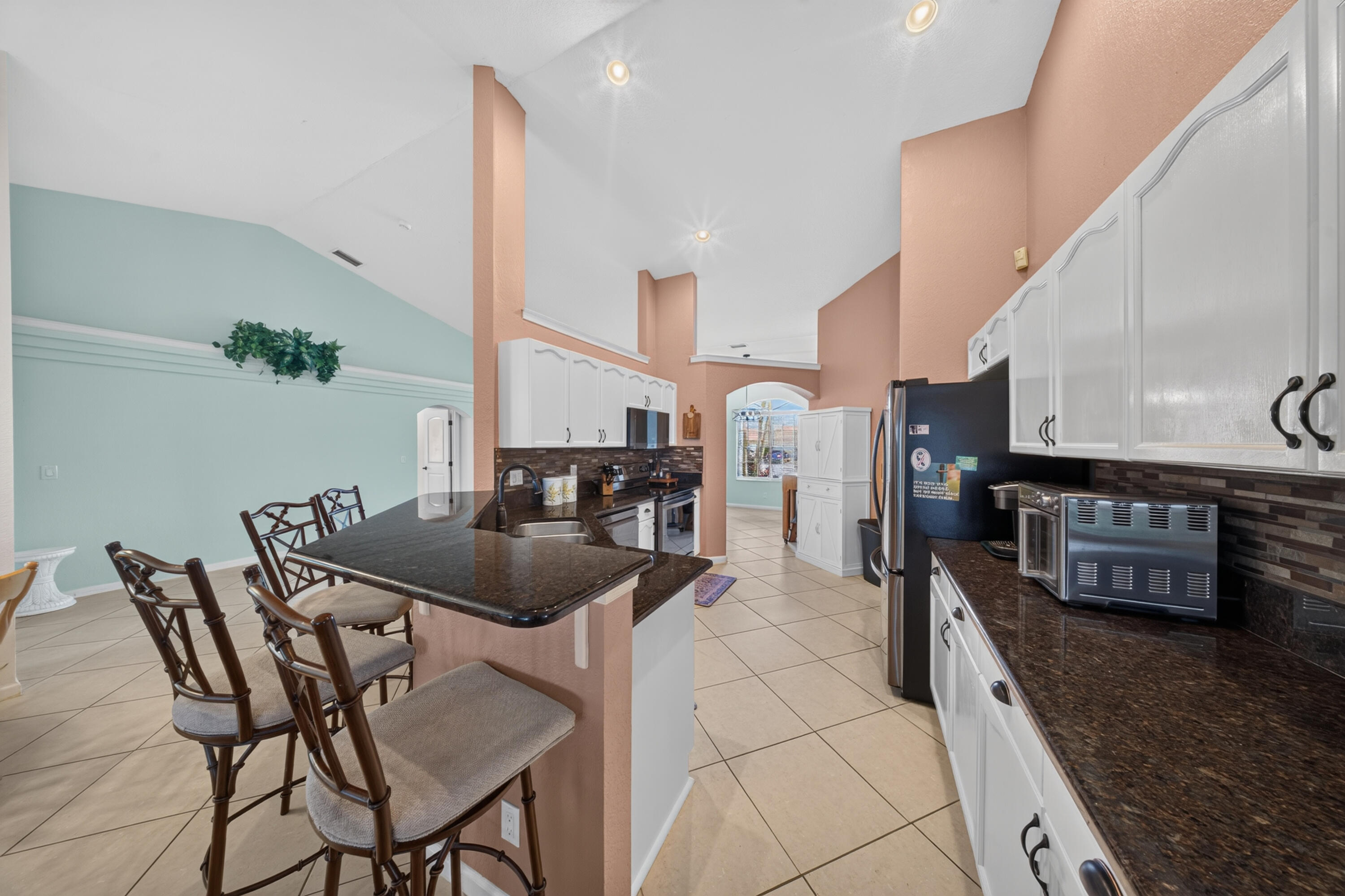 Kitchen featuring white cabinetry, dark countertops, tile flooring, a tile backsplash, and a breakfast bar