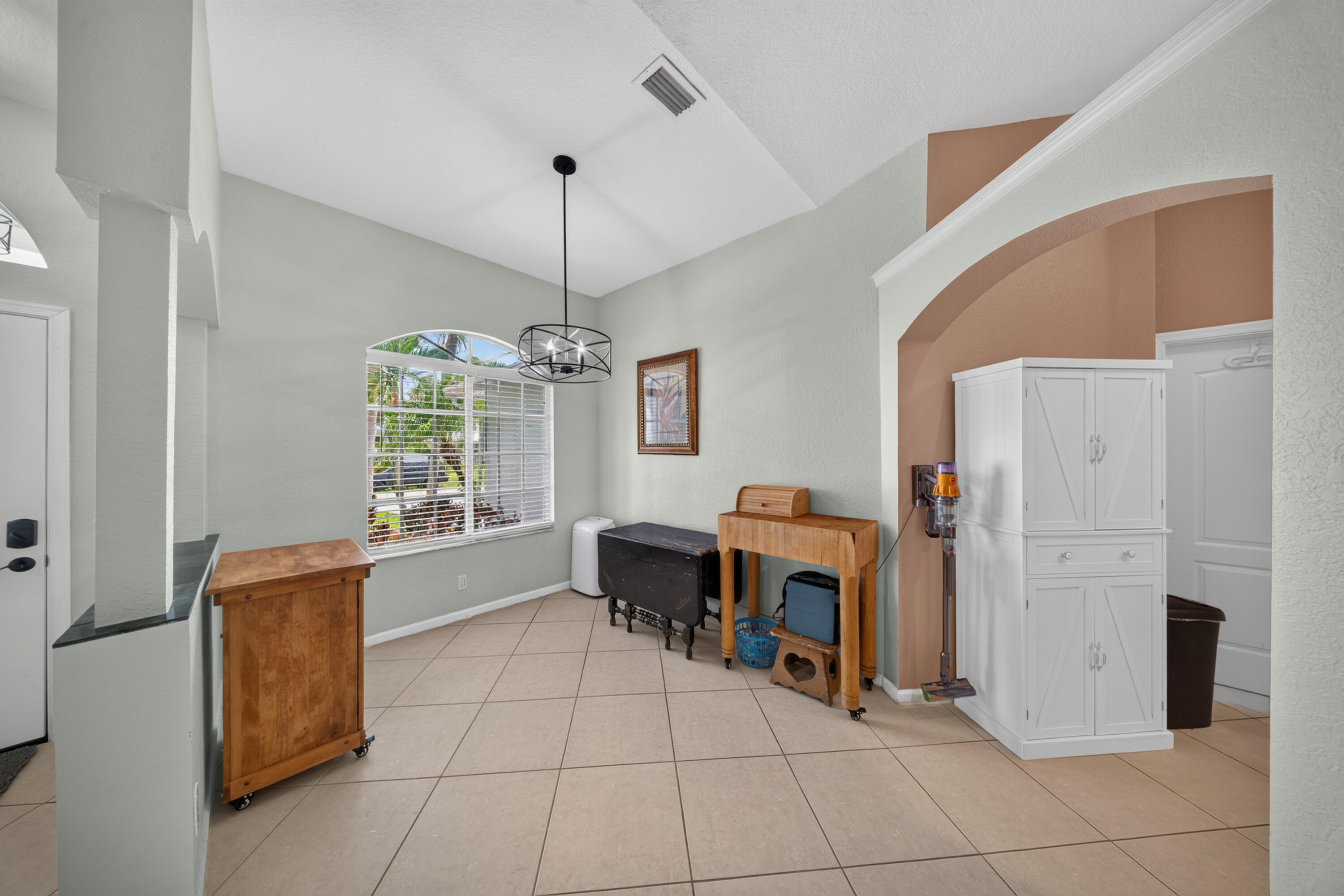Vaulted ceilings, arched wall opening, tiled flooring, an arched window, and a contemporary chandelier