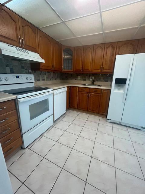 Kitchen featuring wood cabinetry, white appliances, tile flooring, and a tile backsplash