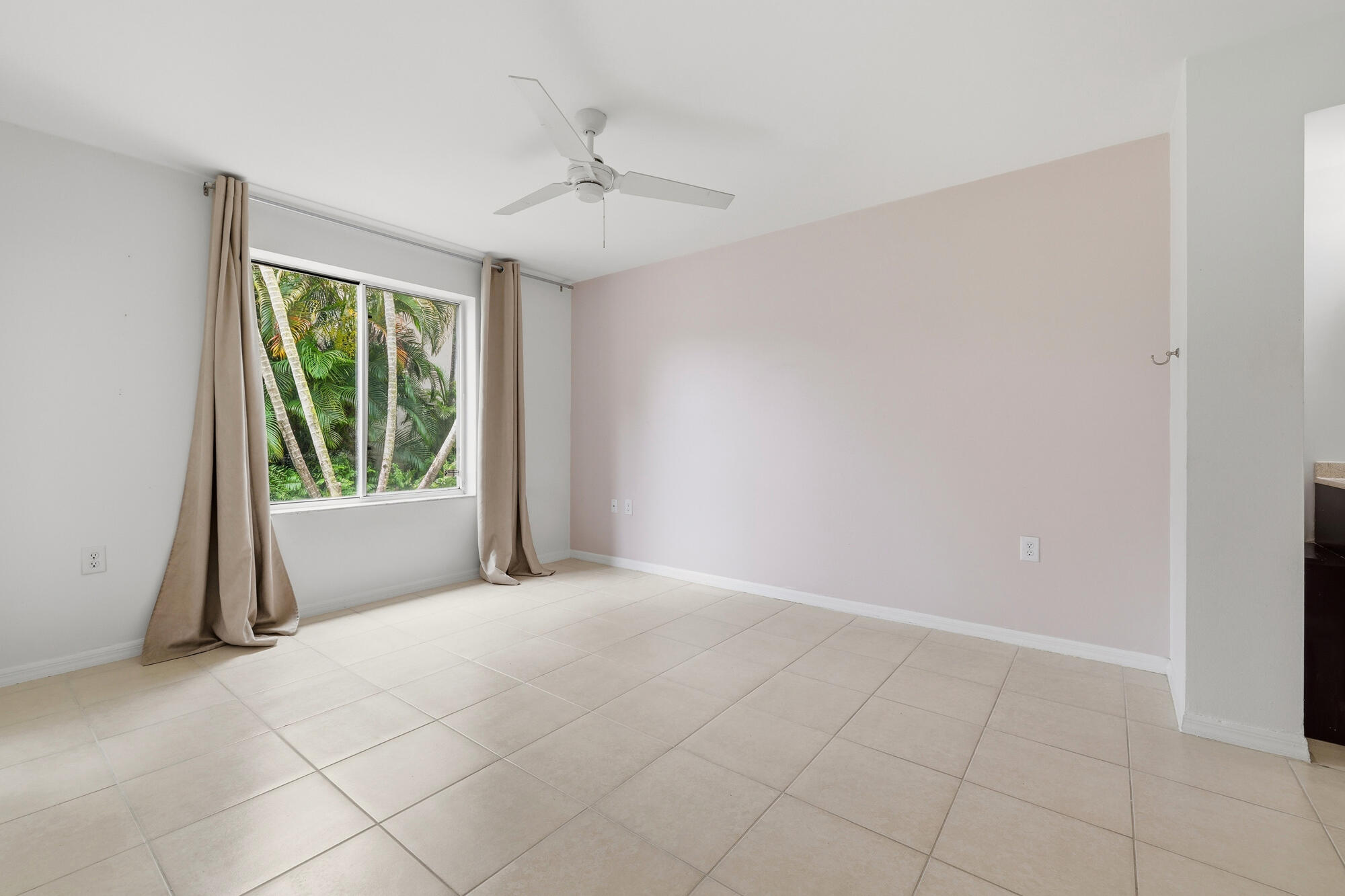 Primary bedroom featuring neutral tile flooring and a large window overlooking lush tropical foliage