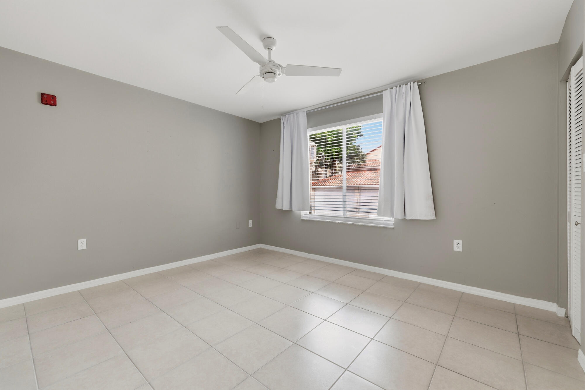 Bedroom two featuring neutral gray walls, beige tile flooring, and a white ceiling fan