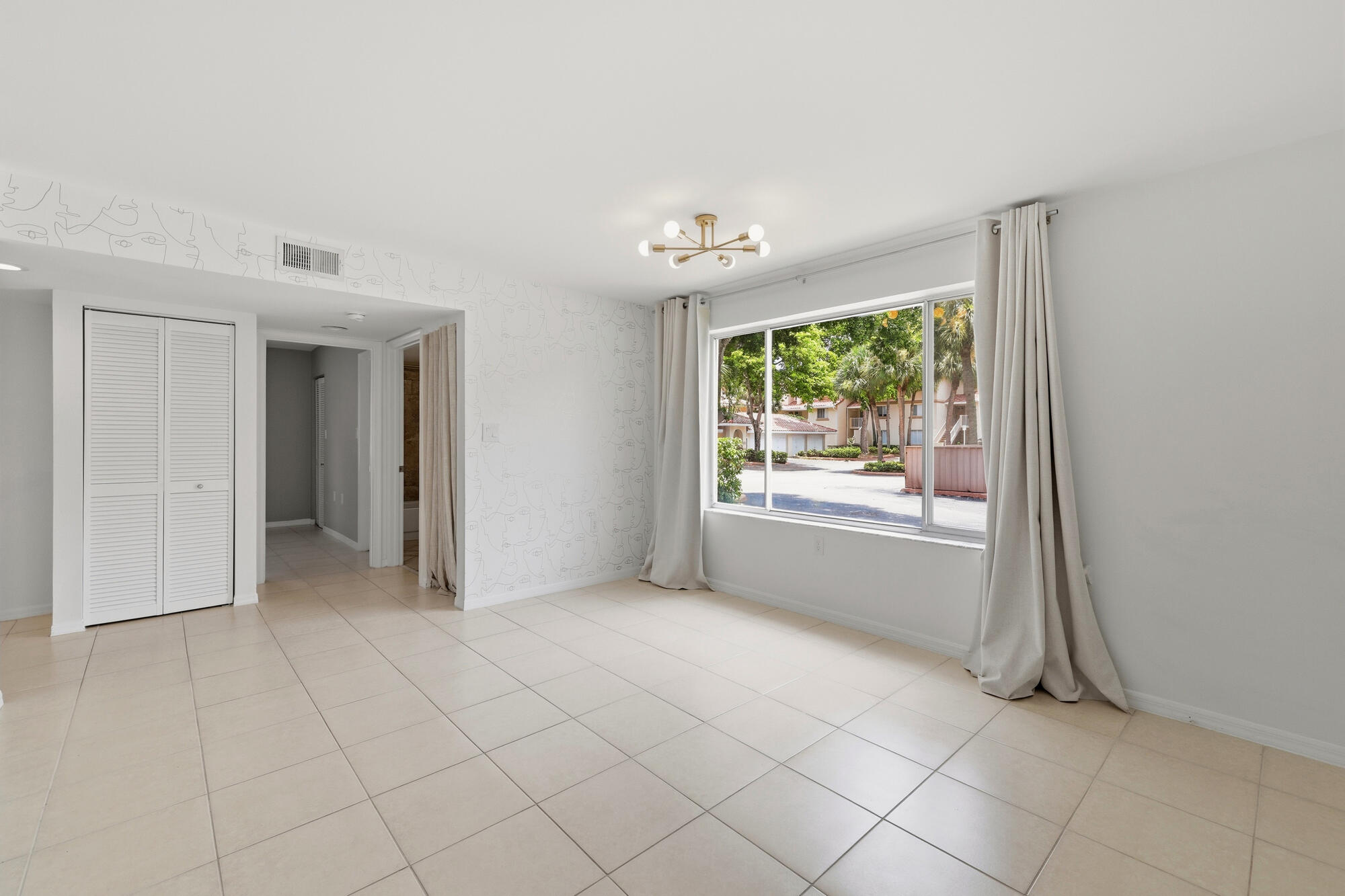 Bright living space featuring large format tile flooring, a modern sputnik light fixture, and a wide window with exterior landscaping